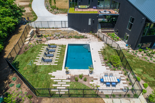 Aerial view of a modern backyard pool with lounge chairs, patio seating, and surrounding greenery.