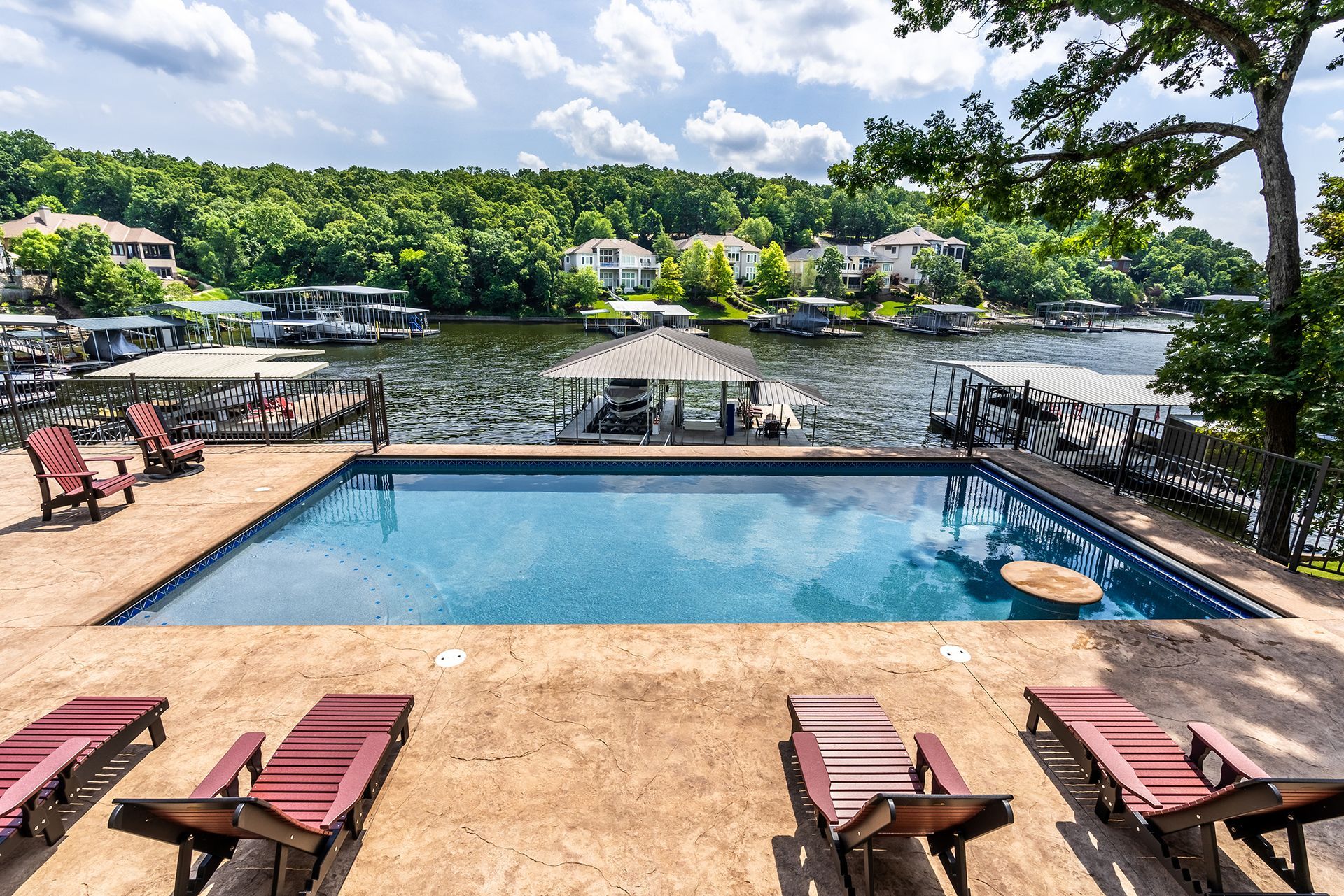 Resort pool overlooking a lake, with lounge chairs, dock, and trees under a partly cloudy sky