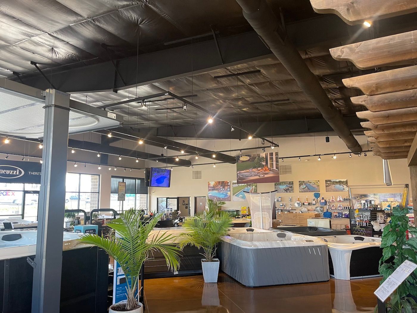 Indoor restaurant showroom with plants, tables, and a high black ceiling under bright lights