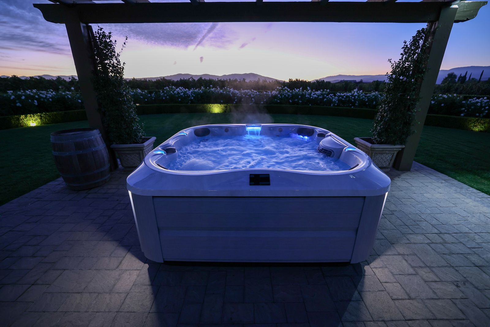 Lit hot tub on a patio at dusk, with blue water jets and a pergola overhead