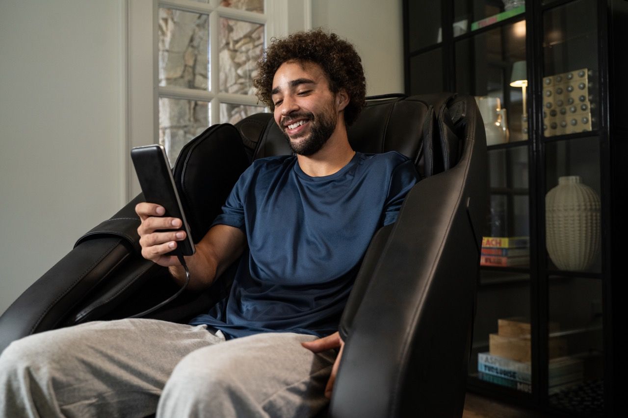 Smiling person sitting in an armchair, looking at a smartphone in a living room