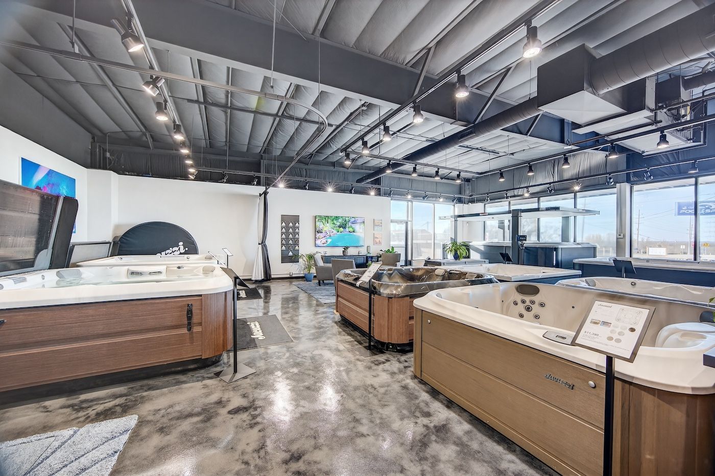 Modern showroom with hot tubs, polished concrete floor, and industrial ceiling beams