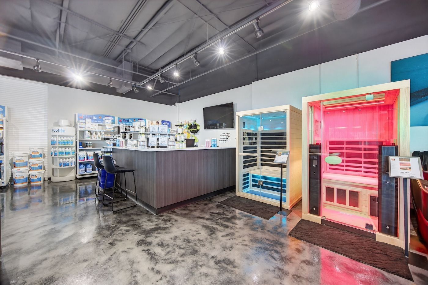 Modern retail interior with a central counter, shelving, and a bright pink fitting room on the right