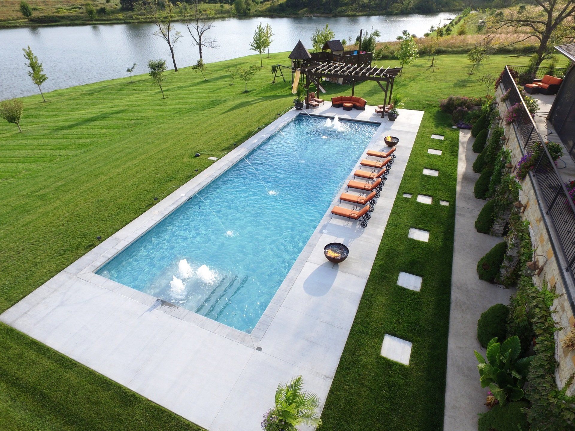 Rectangular backyard pool beside a green lawn, with lounge chairs and a river in the background