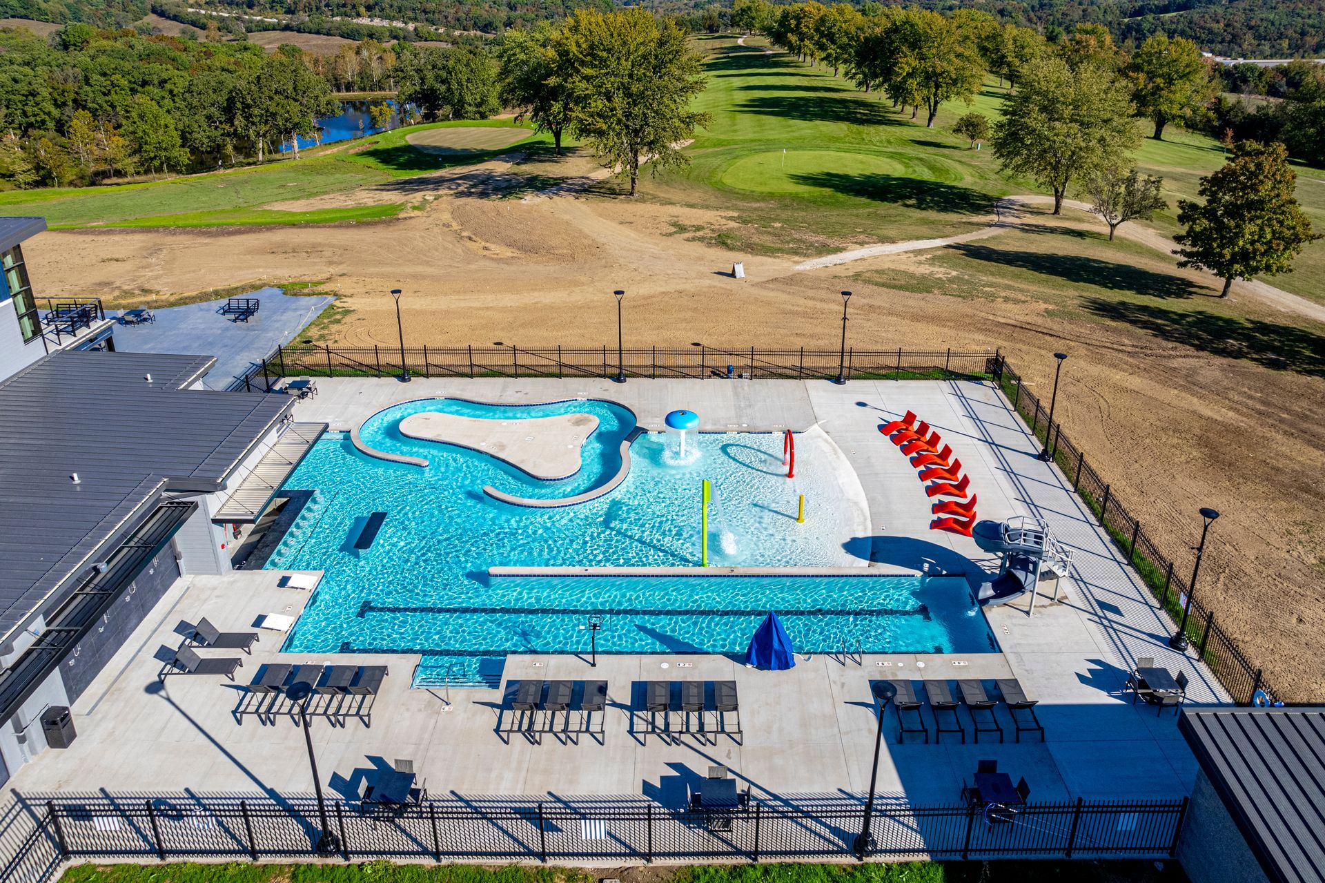 Outdoor swimming pool with blue water slides and red lounge chairs beside a grassy park area