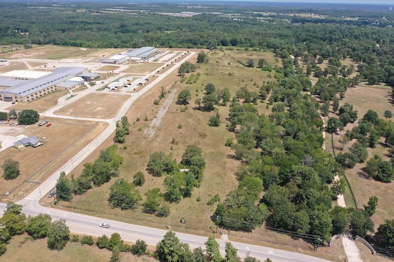 An aerial view of a large field surrounded by trees and a road.