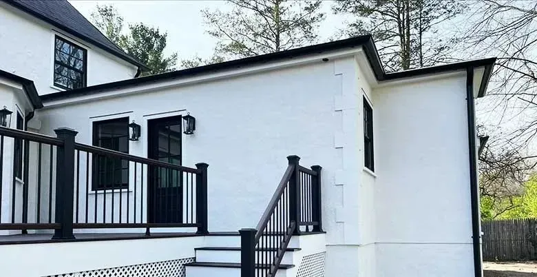 A white house with a black deck and stairs leading up to it.