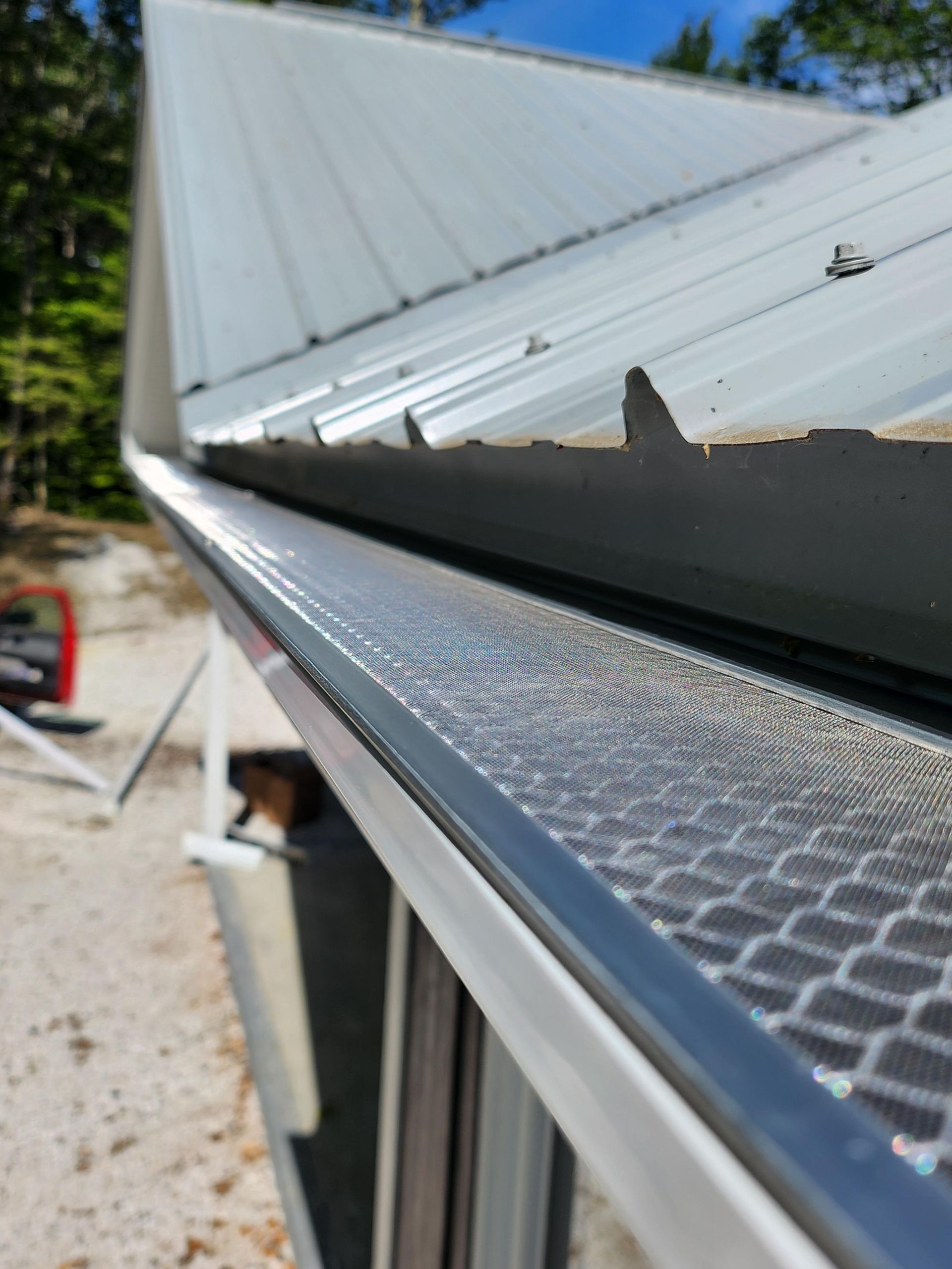Gros plan sur une gouttière métallique avec grille de protection sur un bâtiment à toiture métallique.