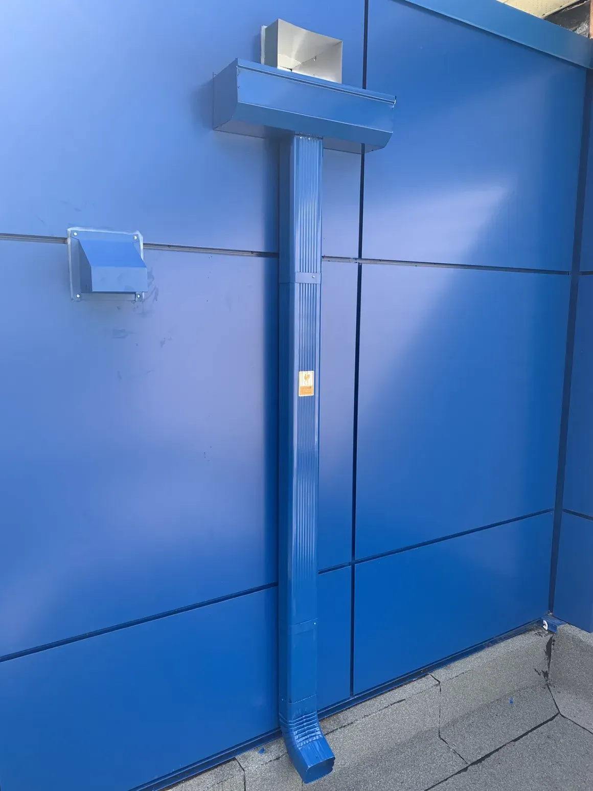A blue drainpipe is attached to a blue wall.