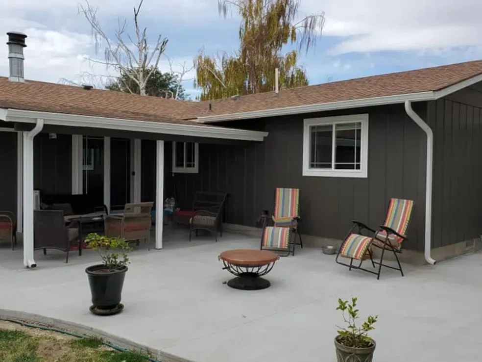 A patio with chairs , a table and a fire pit in front of a house.