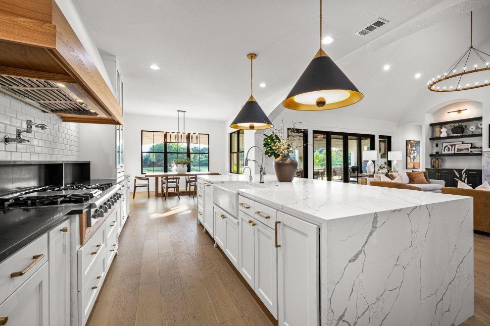 Bright, modern kitchen with white cabinets, marble island, and black/gold pendant lights.