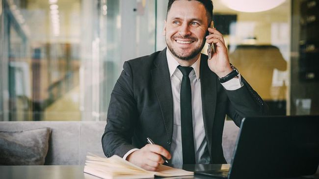 Business owner takes notes at a desk while talking on the phone about business finances.