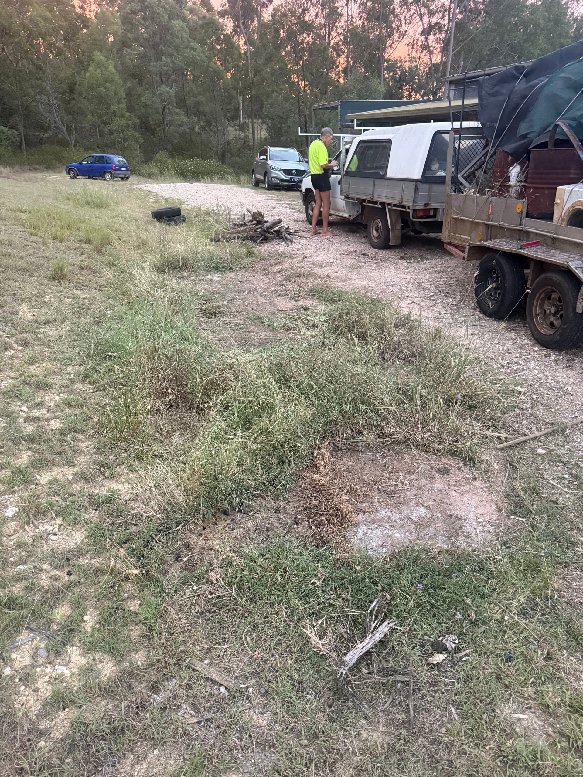 Overgrown grass area with work trucks and workmen. Sunset in Toowoomba
