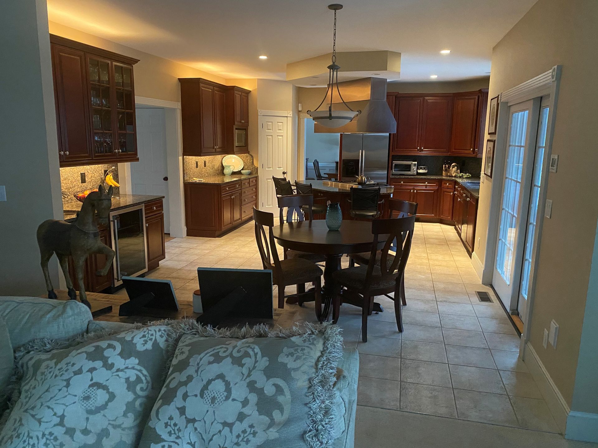 Open-concept kitchen and dining room with wood cabinets, pendant light, and tiled floor viewed from a living room.