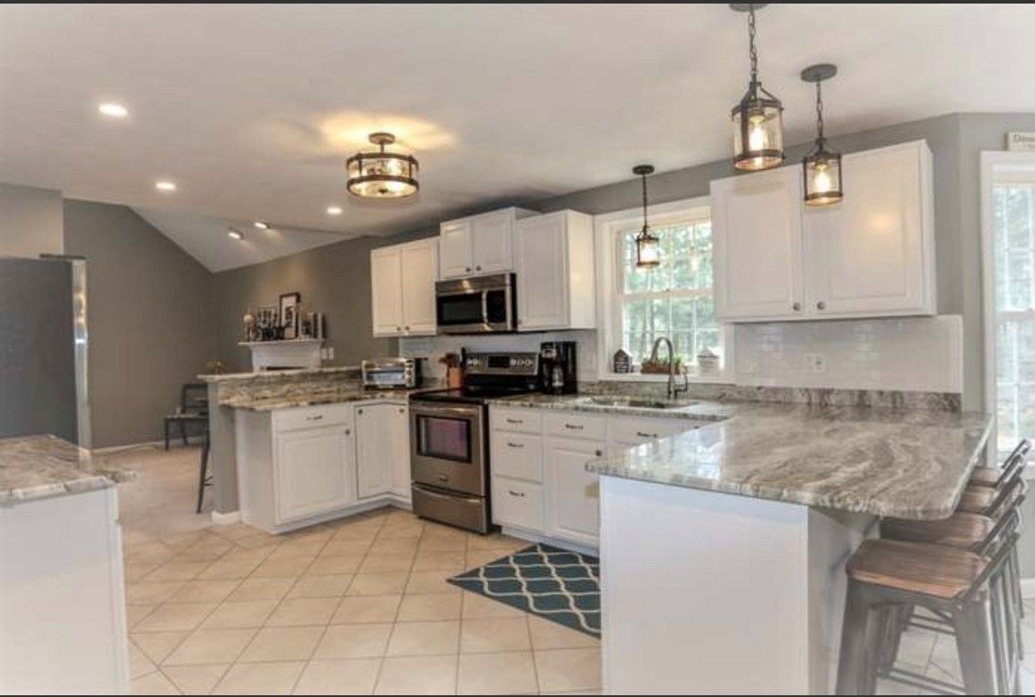 Bright kitchen with white cabinets, granite counters, stainless stove, and tiled floor