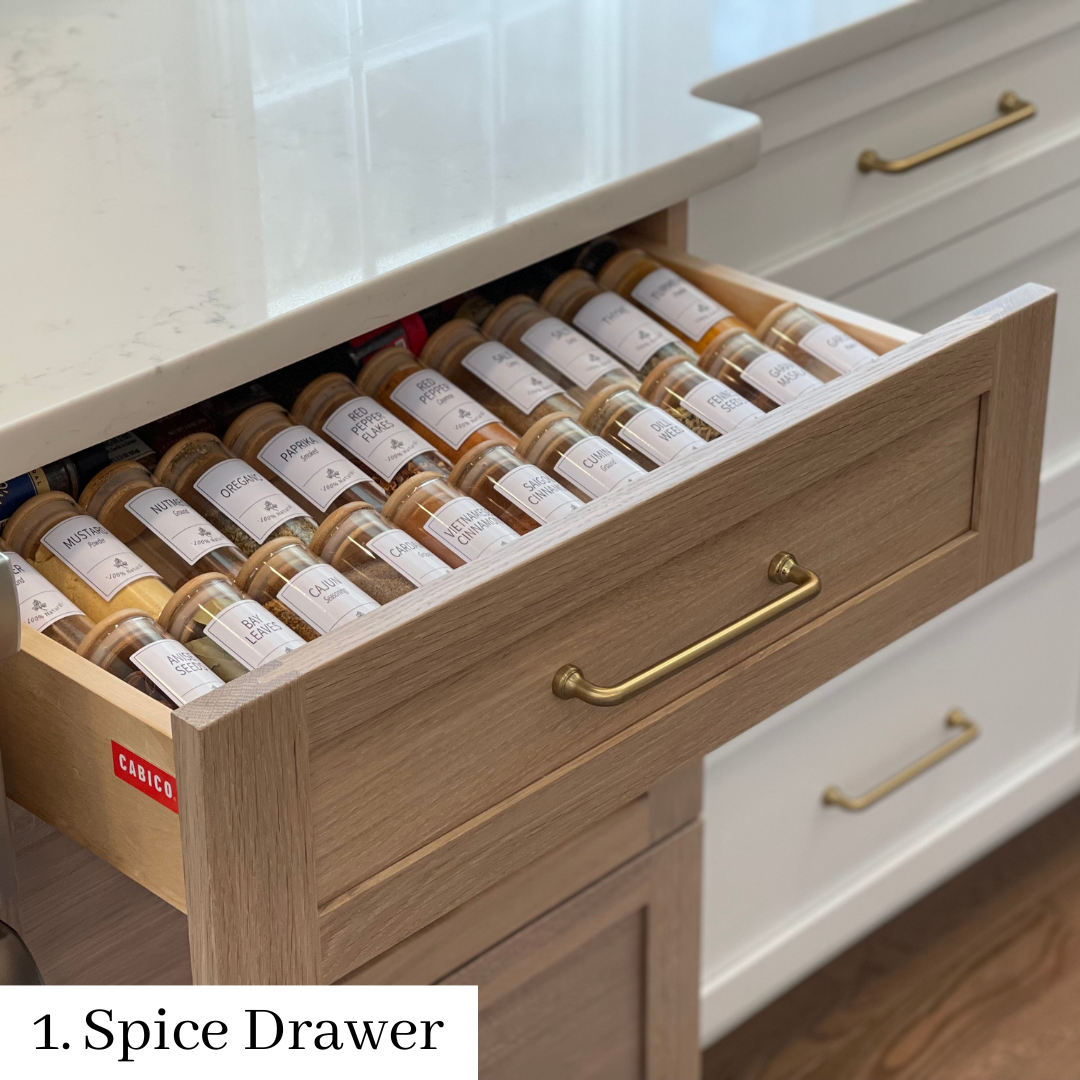 Open spice drawer with neatly arranged labeled jars in a kitchen counter.