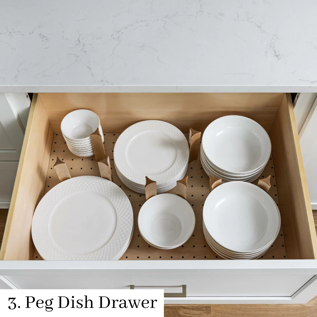 Open kitchen drawer with white dishes organized on peg dividers and a mug at left.