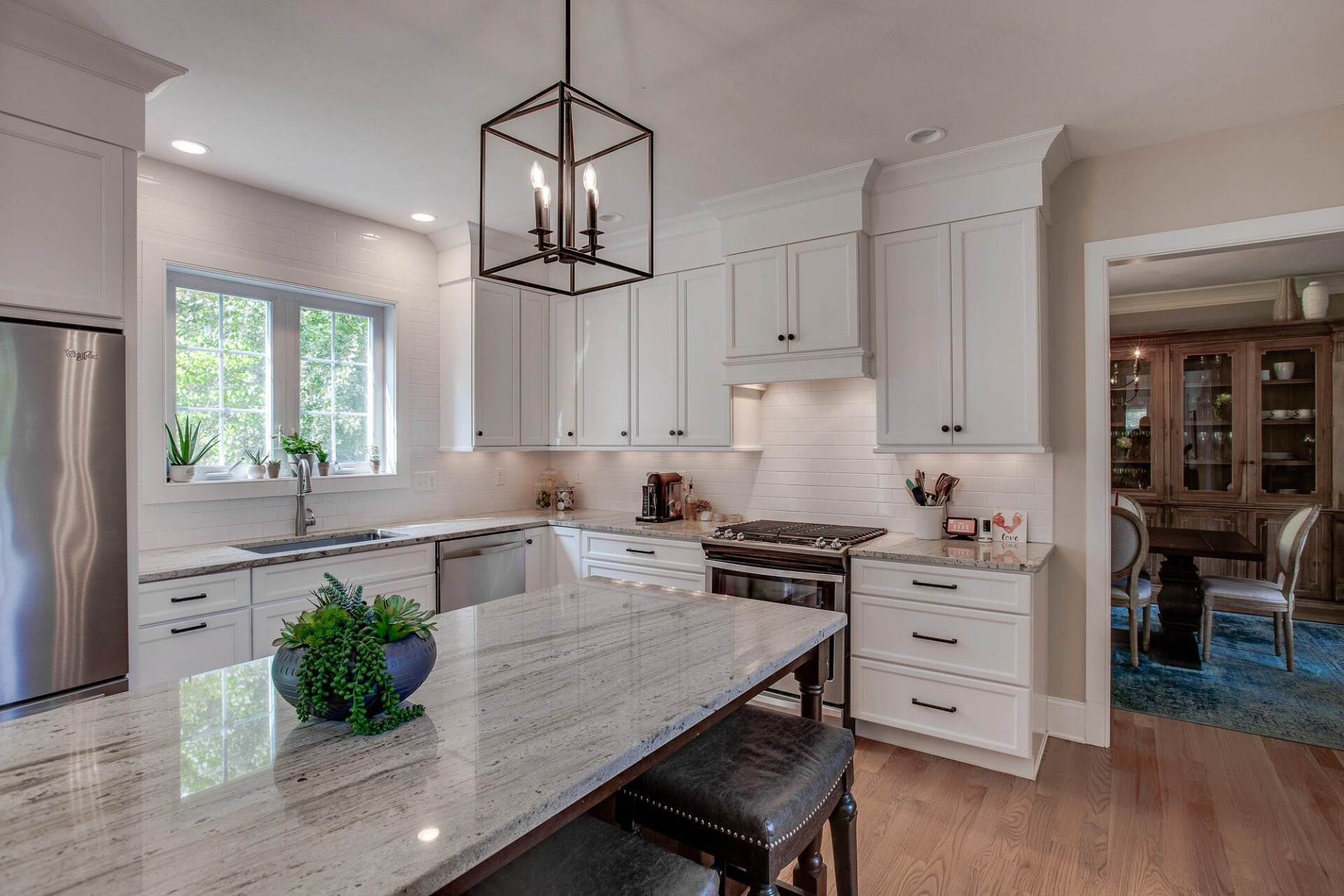 Bright modern kitchen with white cabinets, granite island, pendant light, and stainless steel appliances