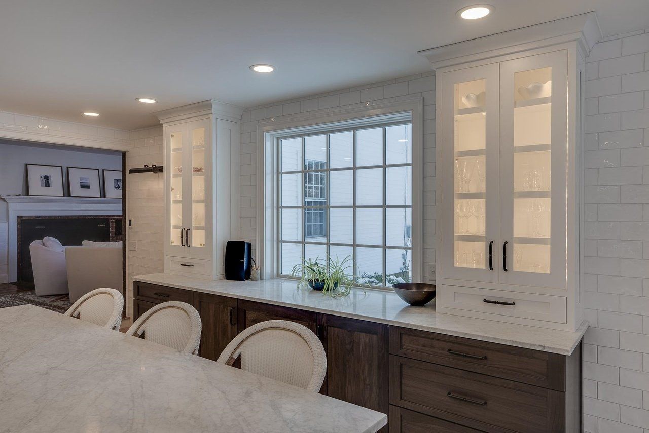 Bright kitchen with white cabinets, a large window, and a dark island with stools.