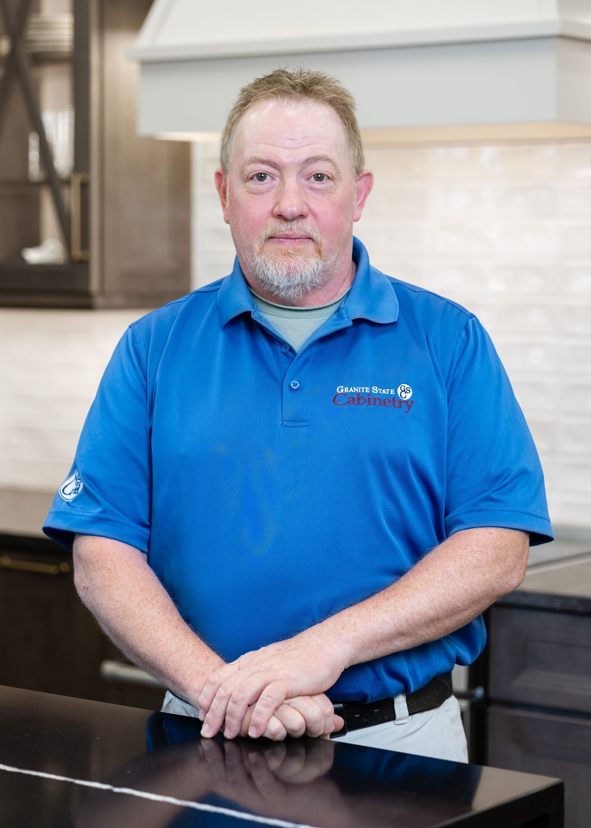 Portrait of a bald man wearing glasses and a navy shirt, standing indoors by a kitchen counter