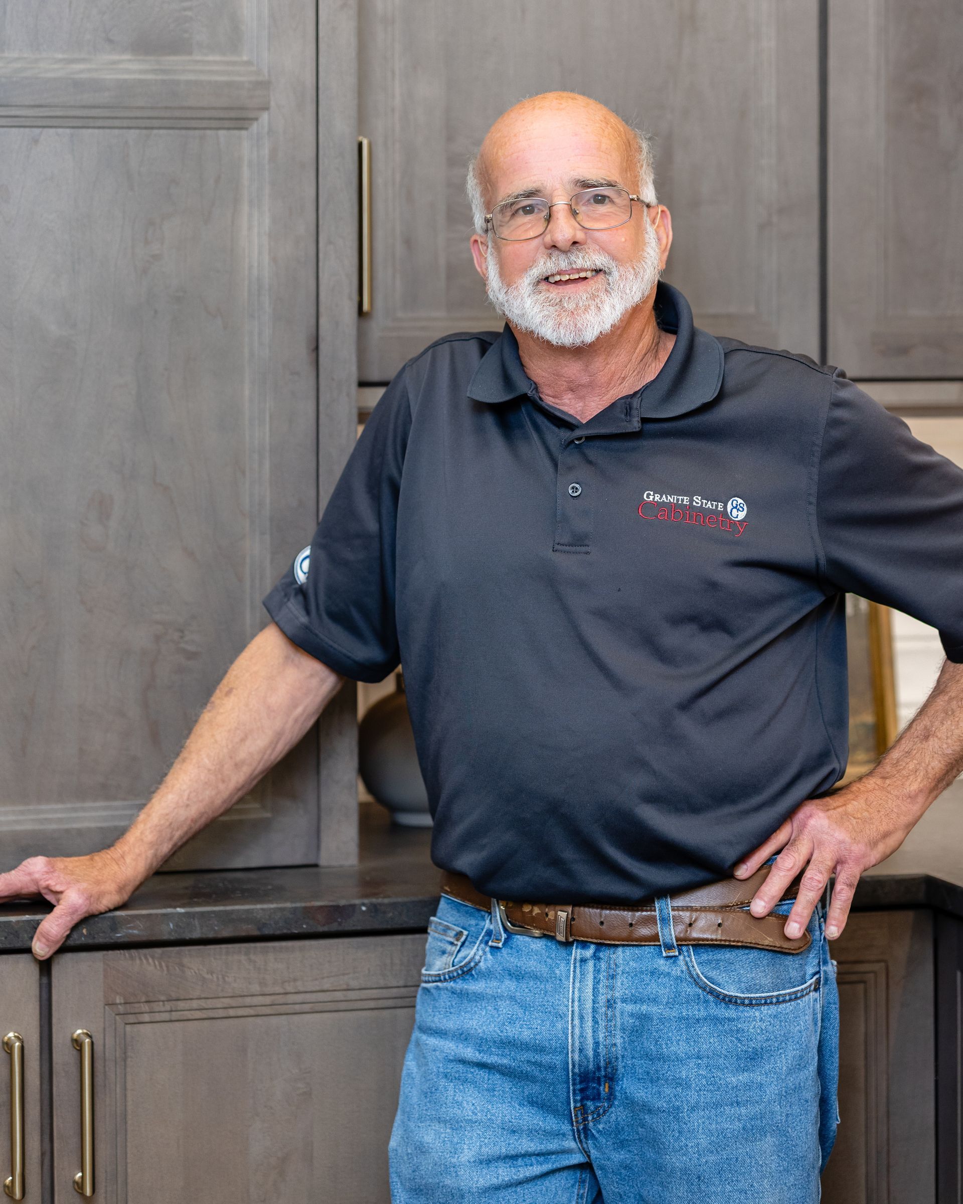 Smiling man in glasses and navy polo shirt standing in a bright kitchen