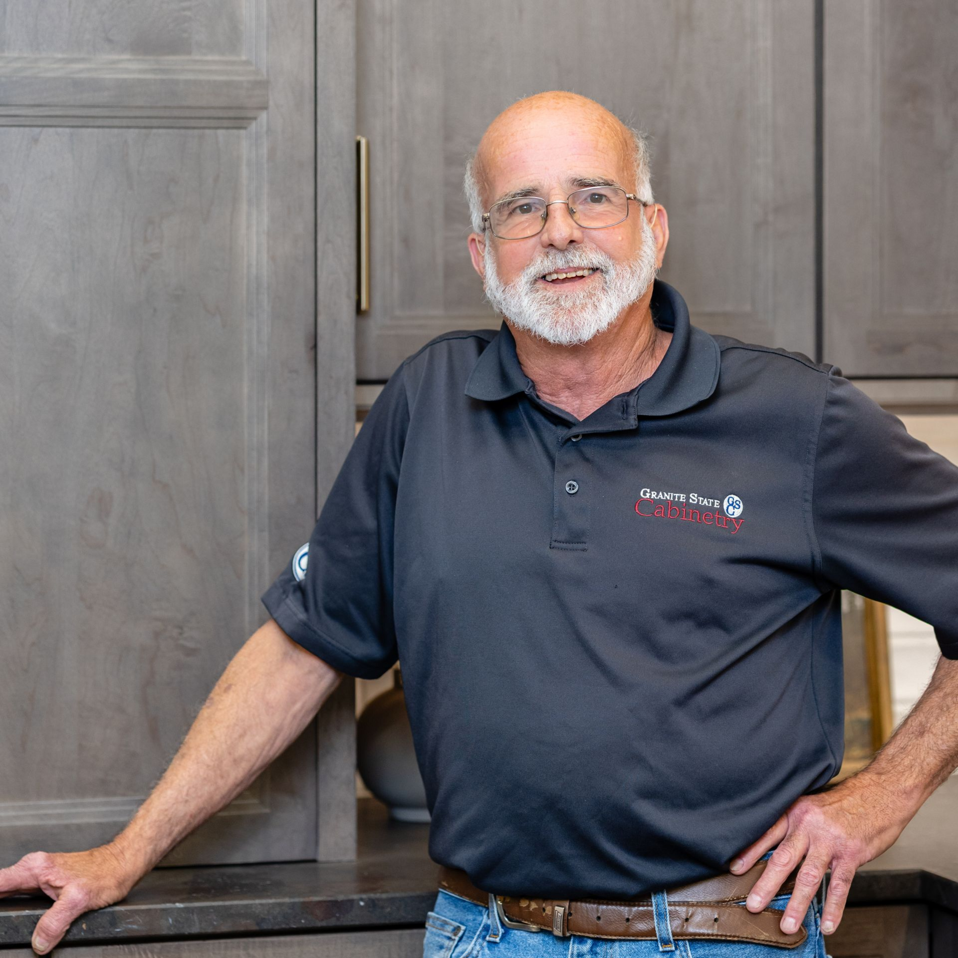 Smiling bald man with glasses in a kitchen, wearing a dark polo shirt.