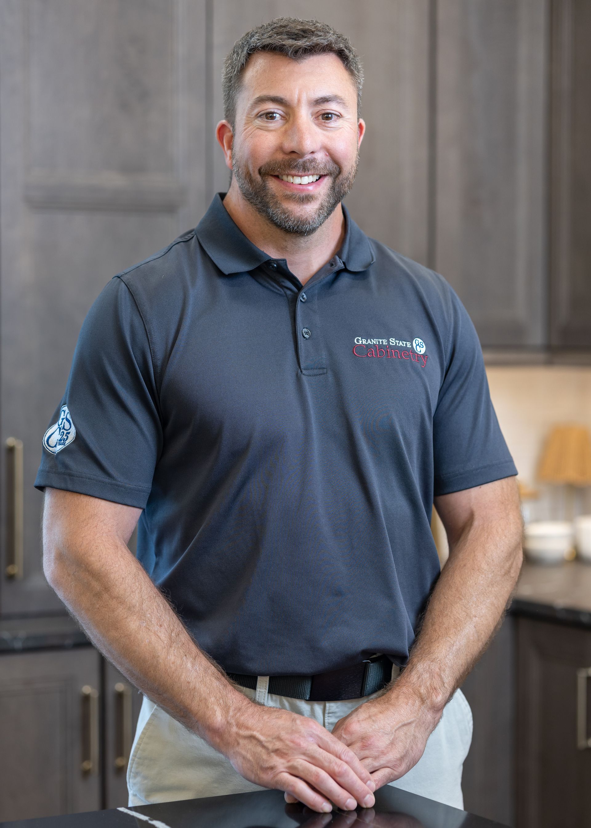 Smiling man in a dark polo shirt standing in a bright kitchen-like interior.