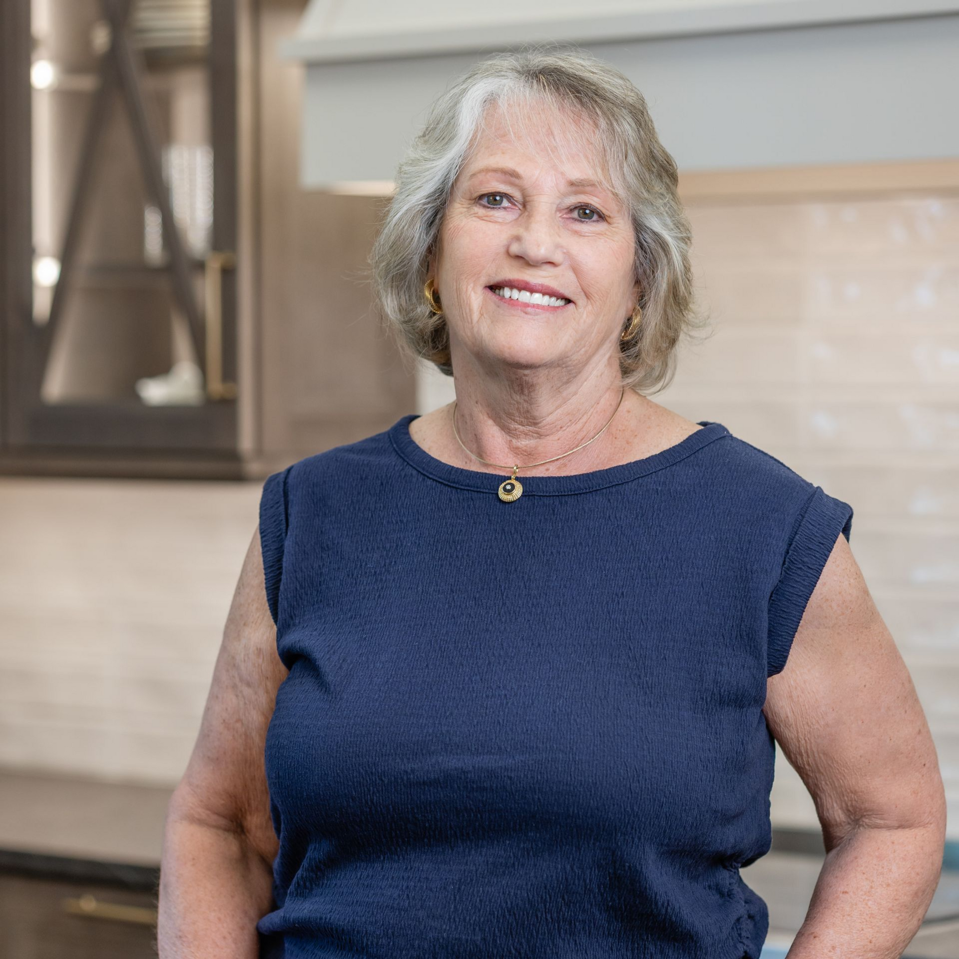 Portrait of a smiling woman in a black top, standing in a bright kitchen