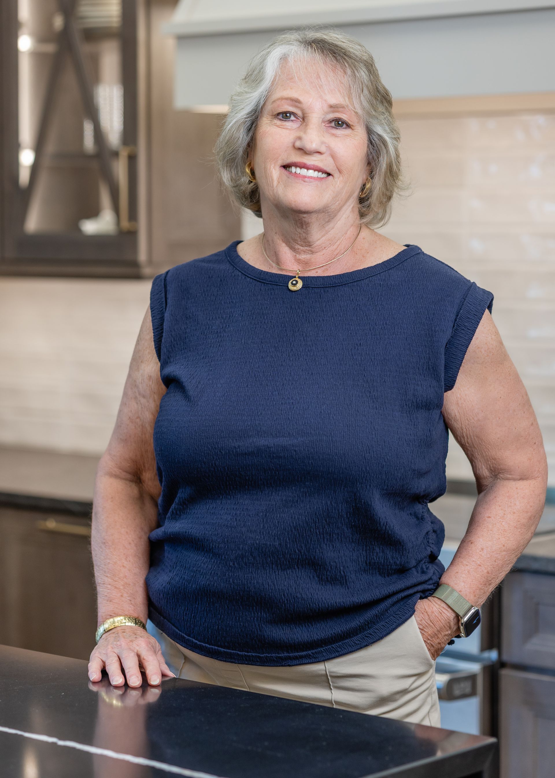 Woman in a black top smiling in a bright kitchen with white cabinets and a marble backsplash