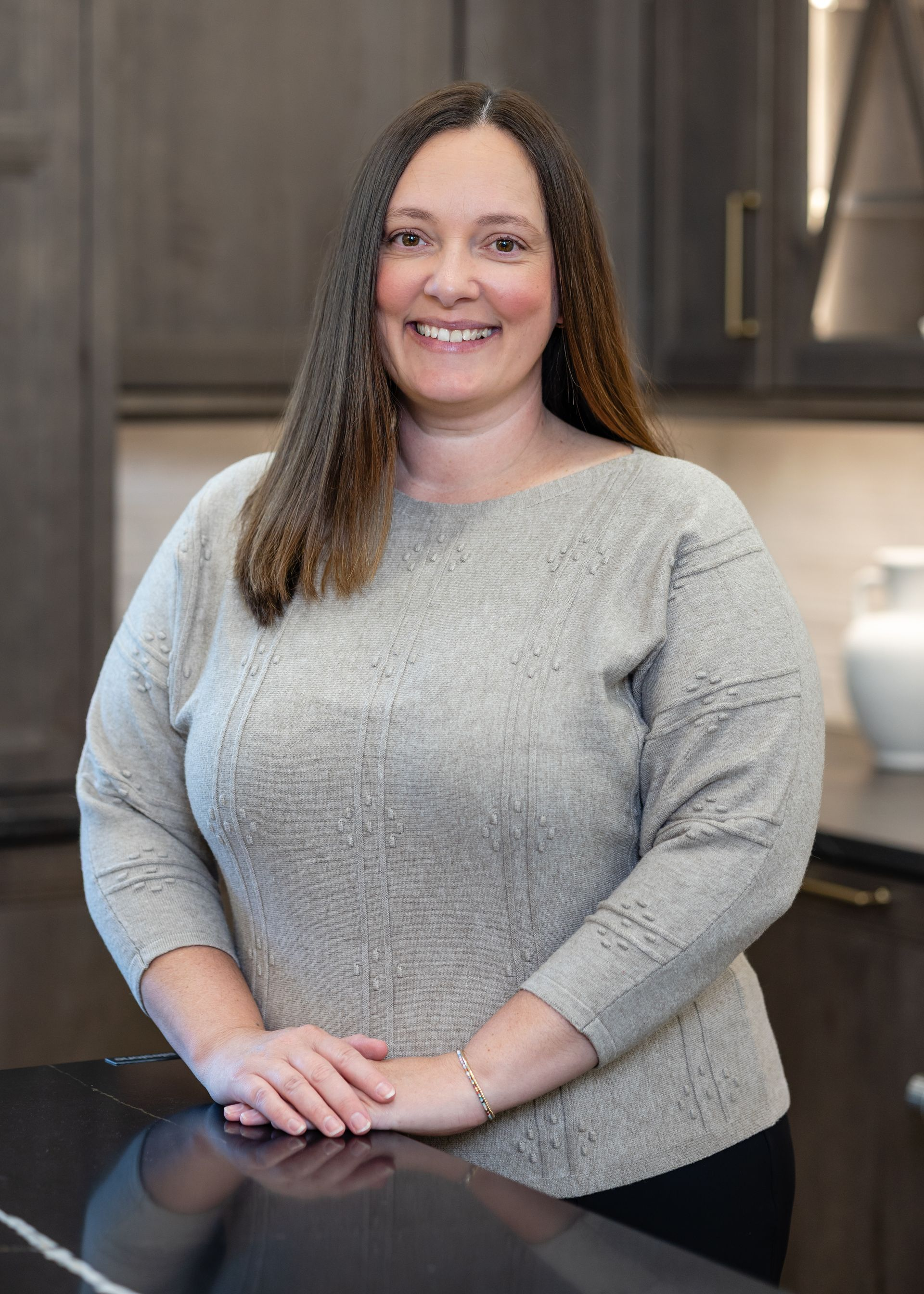 Smiling woman in a white top with long brown hair standing in a bright kitchen