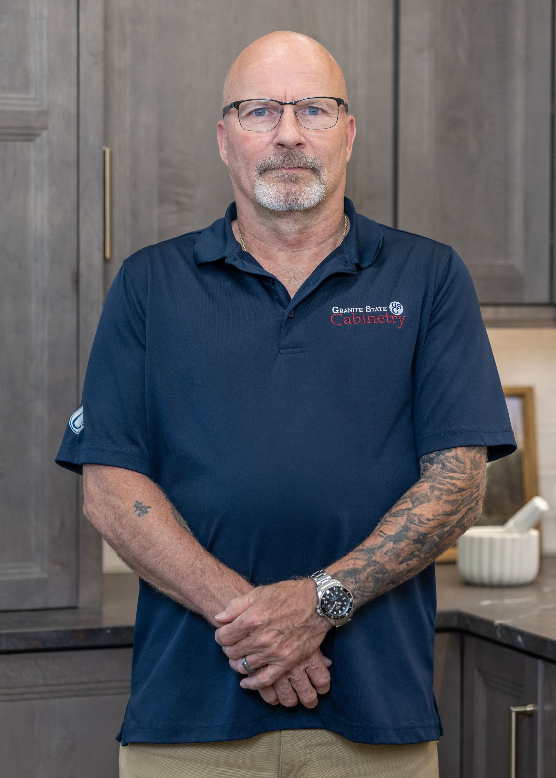 Smiling man in a navy polo shirt standing in a bright kitchen with marble countertops
