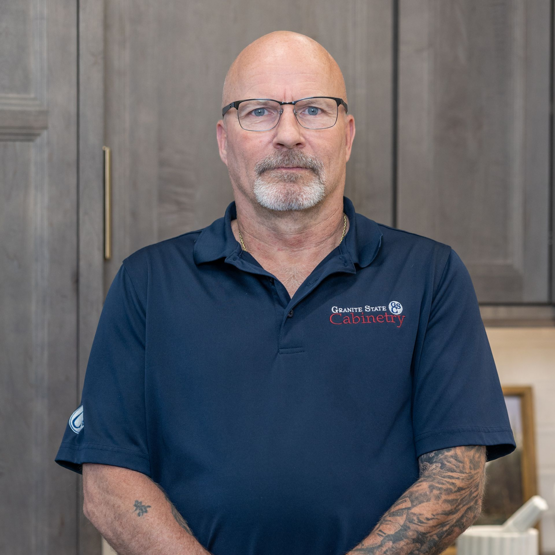 Smiling bald man with glasses in a navy shirt in a bright kitchen