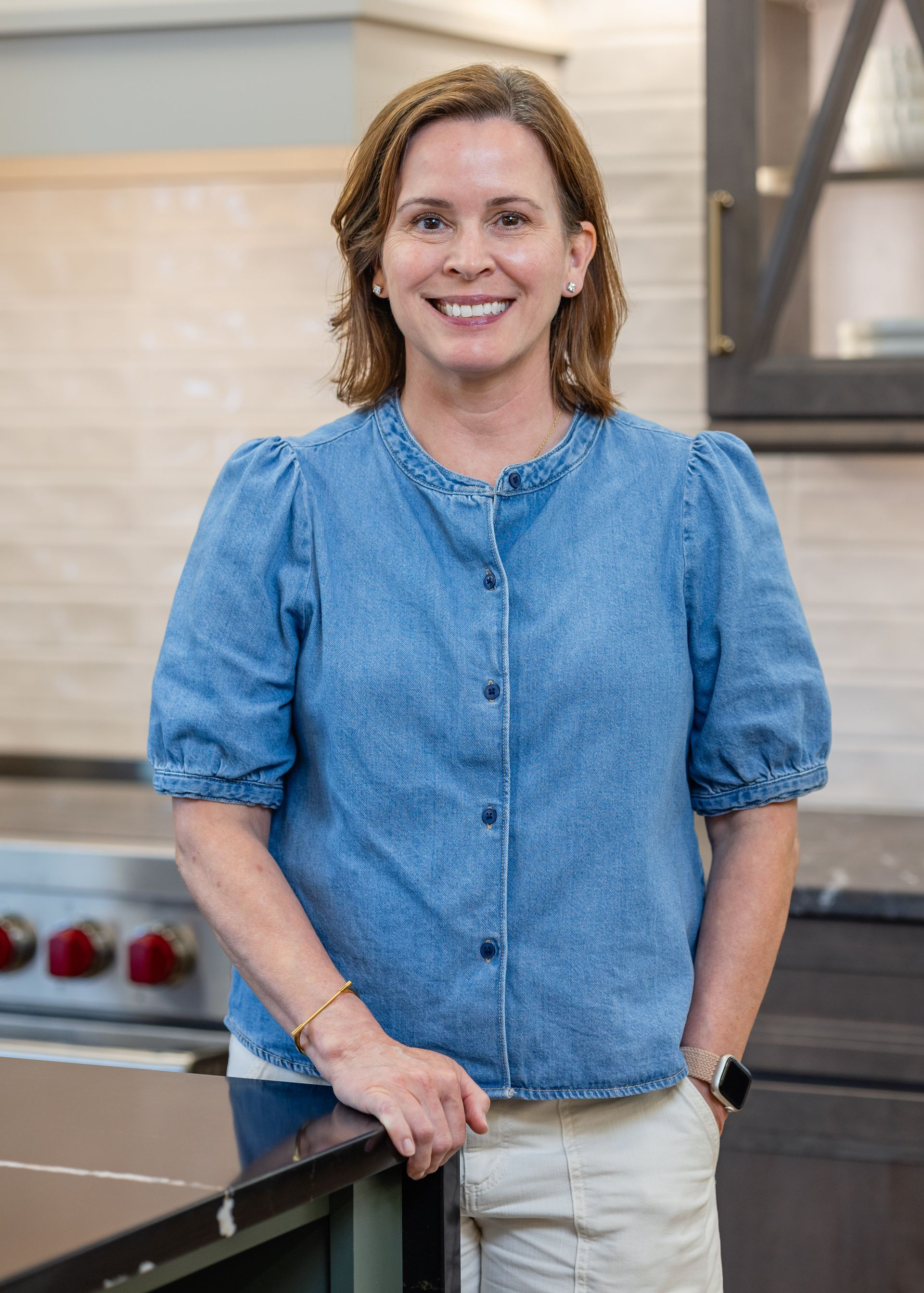 Woman smiling in a kitchen with marble backsplash and shelves in the background