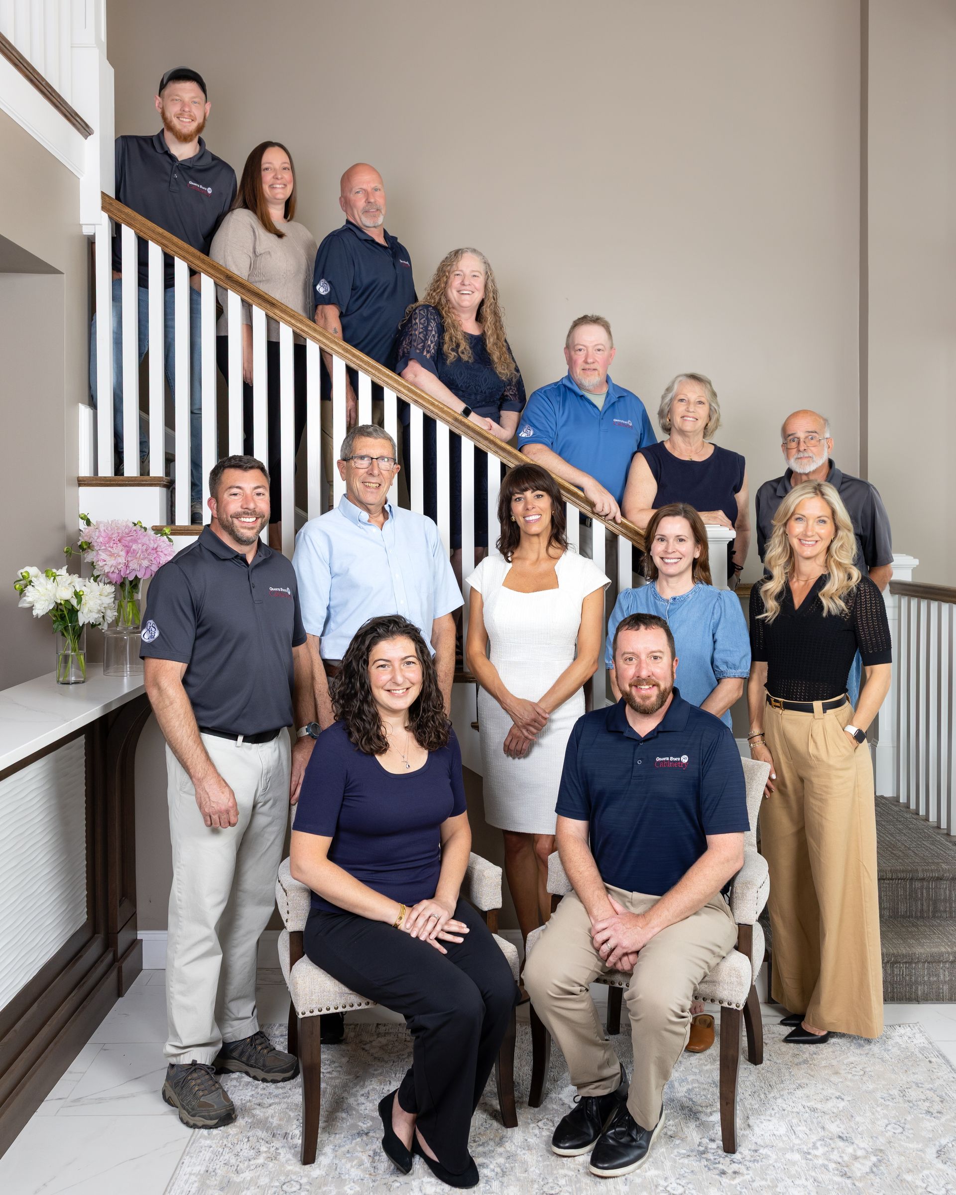 Group of eight people posing in front of a granite state cabinet showroom sign
