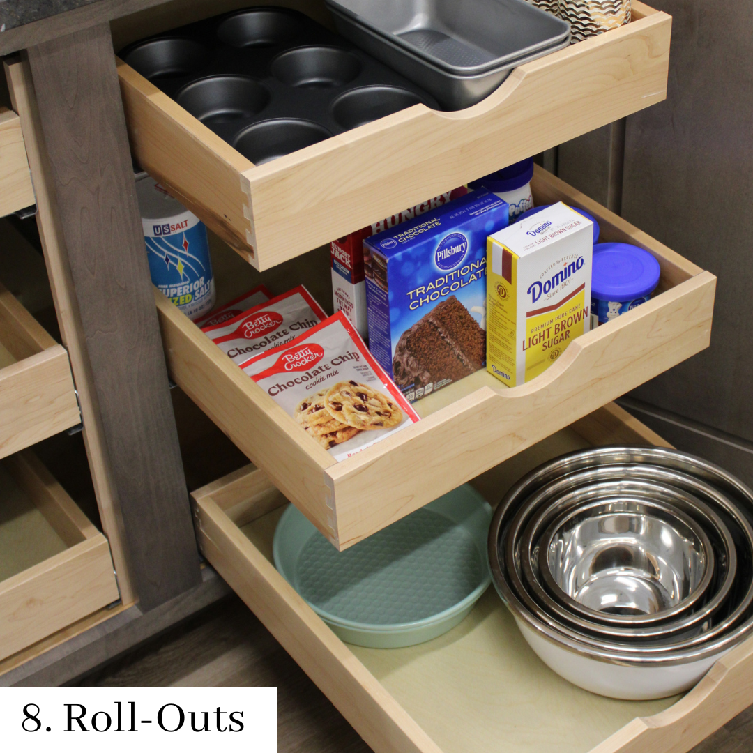 Wooden kitchen pull-out shelves holding baking pans, boxed mixes, a bowl, and stacked metal mixing bowls