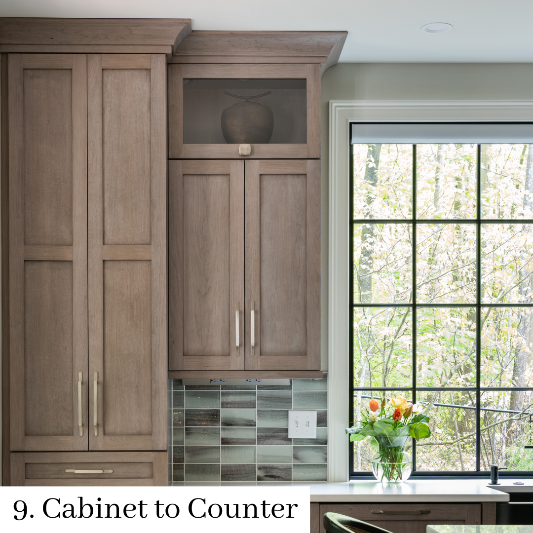 Wood kitchen cabinets beside a window with a vase of orange flowers on the counter