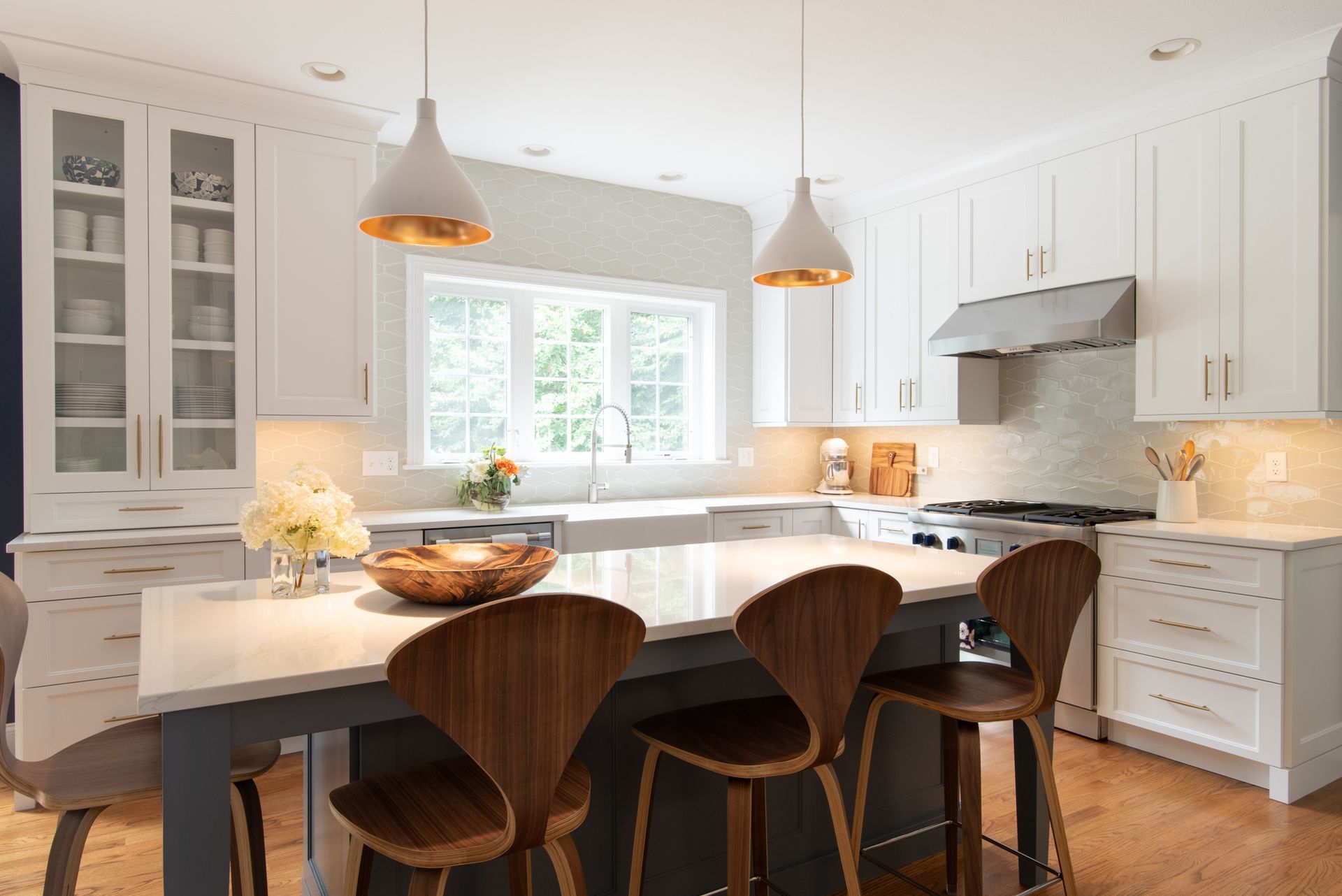 Bright white kitchen with island, wooden stools, pendant lights, and large window over the sink.