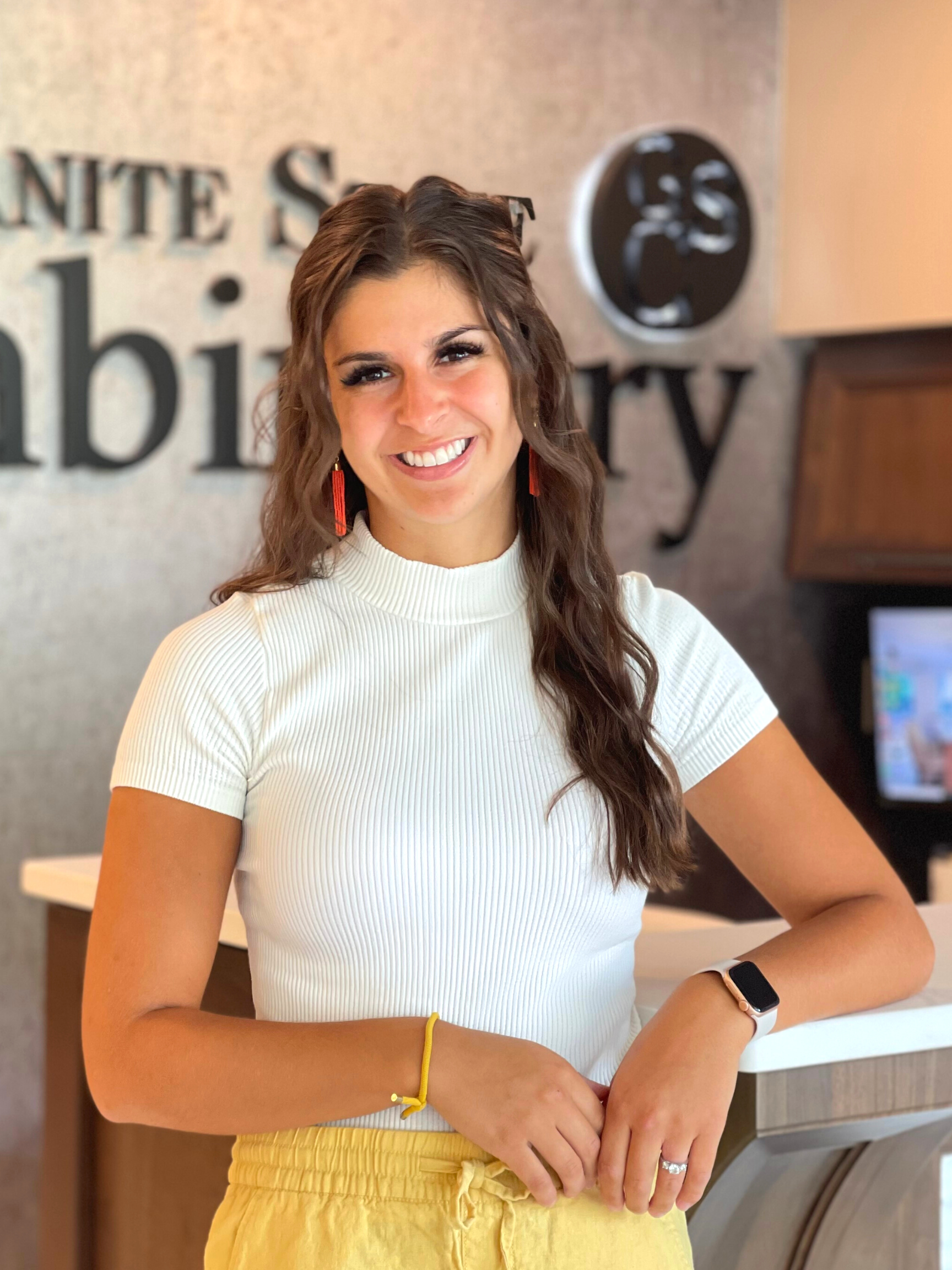 Smiling woman in a white top leaning on a counter in an office lobby.