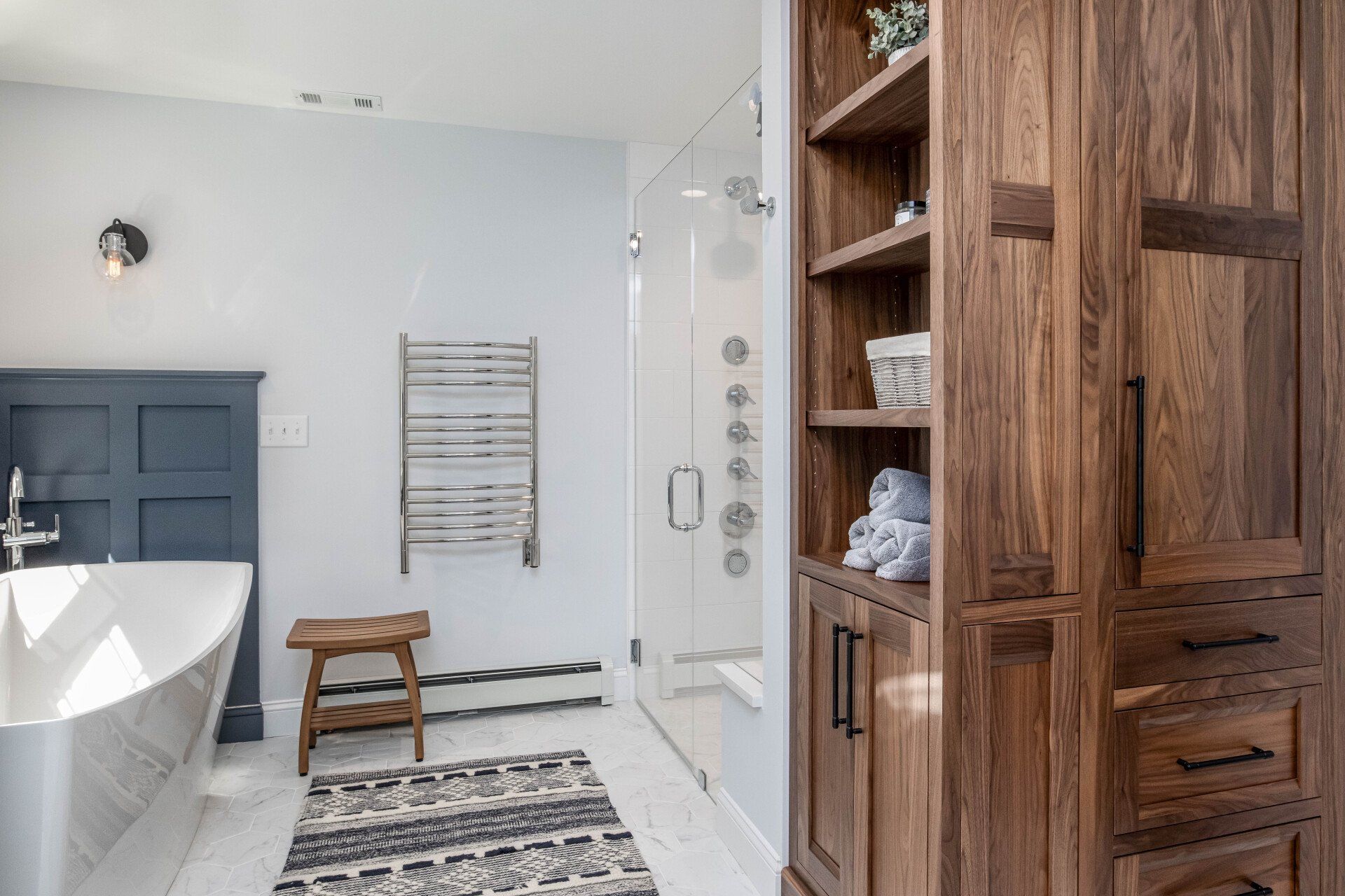 Modern bathroom with freestanding tub, walk-in shower, wooden cabinet, and patterned rug