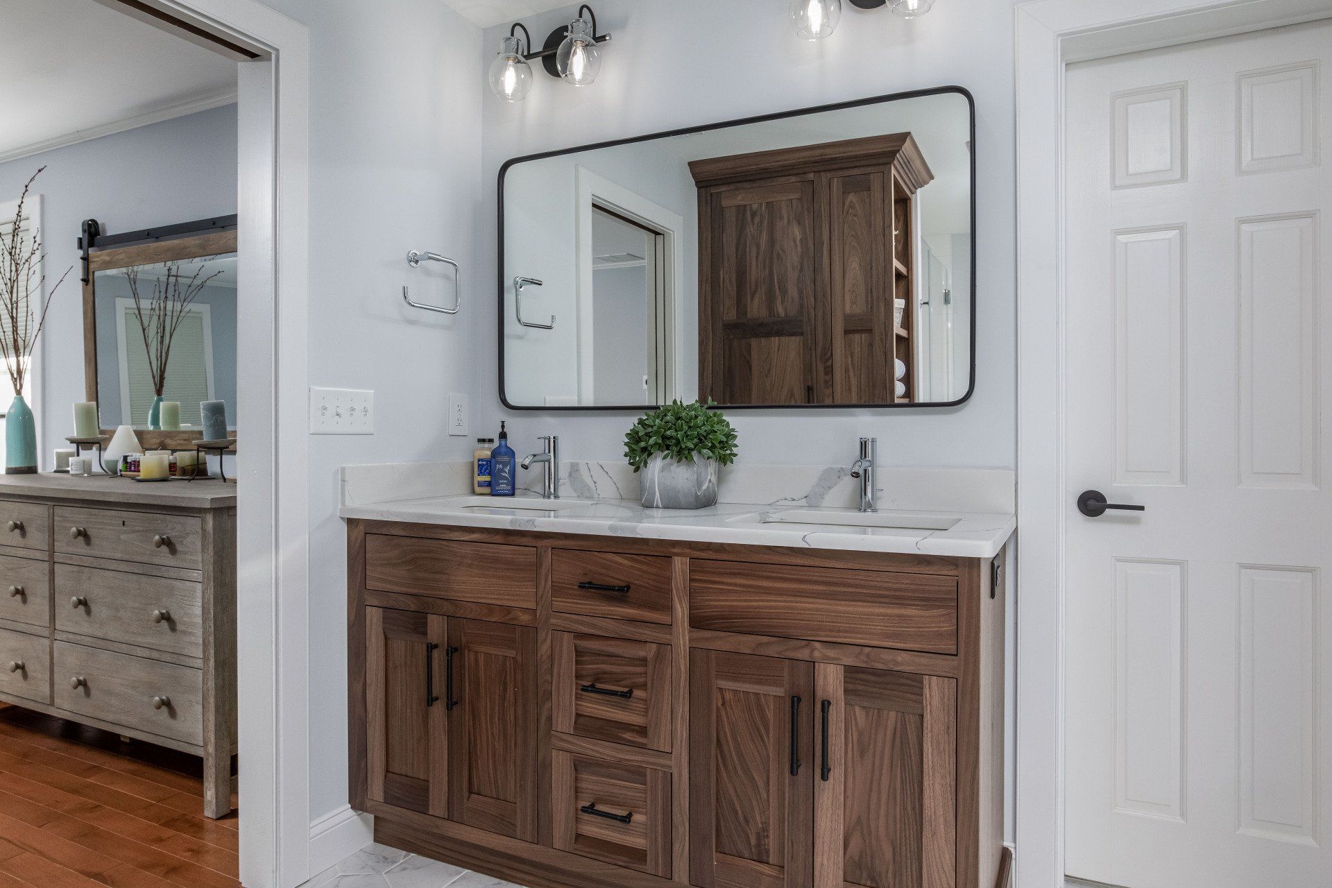 Bathroom vanity with wooden cabinets, large mirror, wall sconce, and white door in a bright room