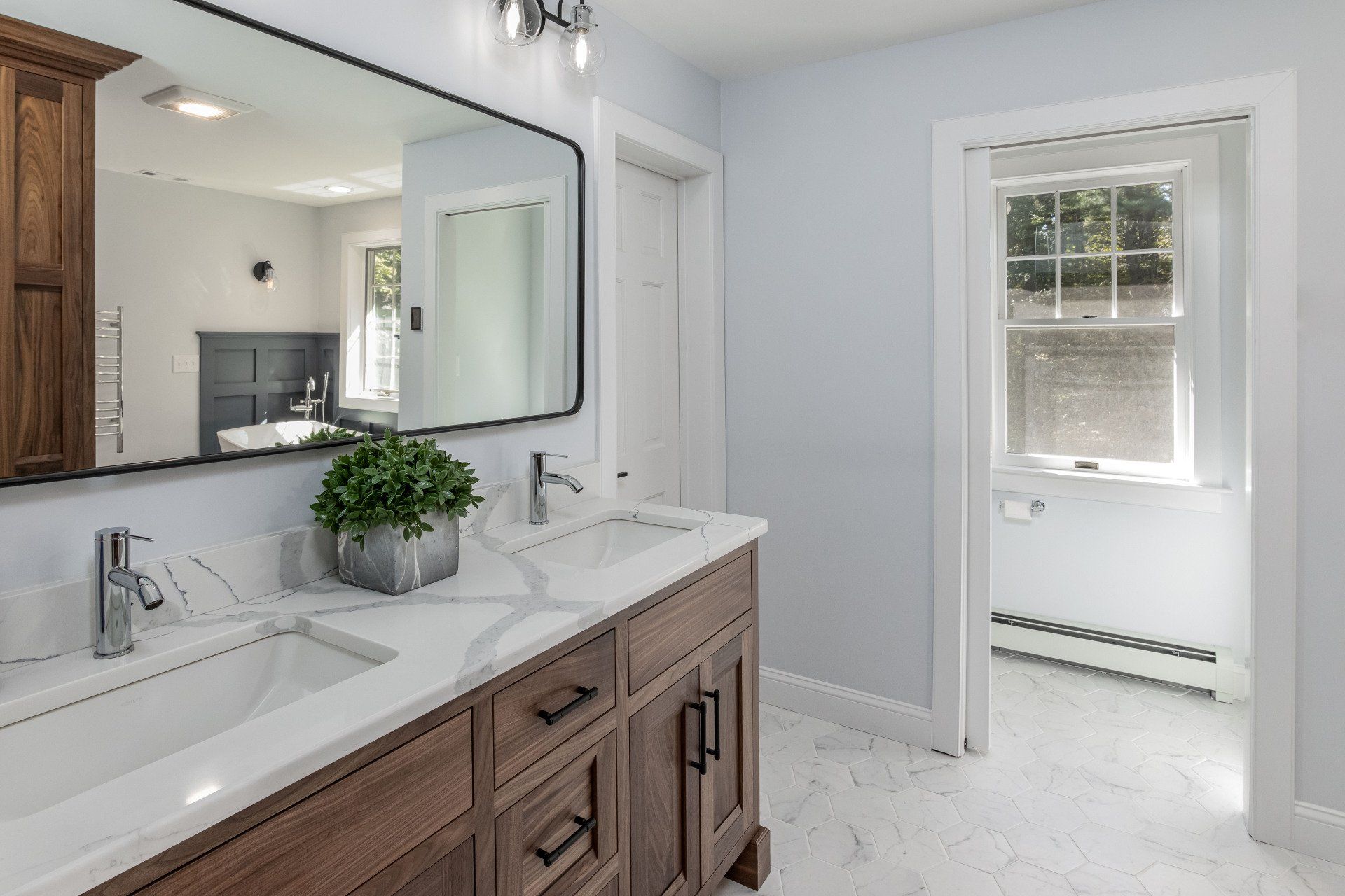 Bright bathroom with double vanity, large mirror, and window beside a white-walled shower area