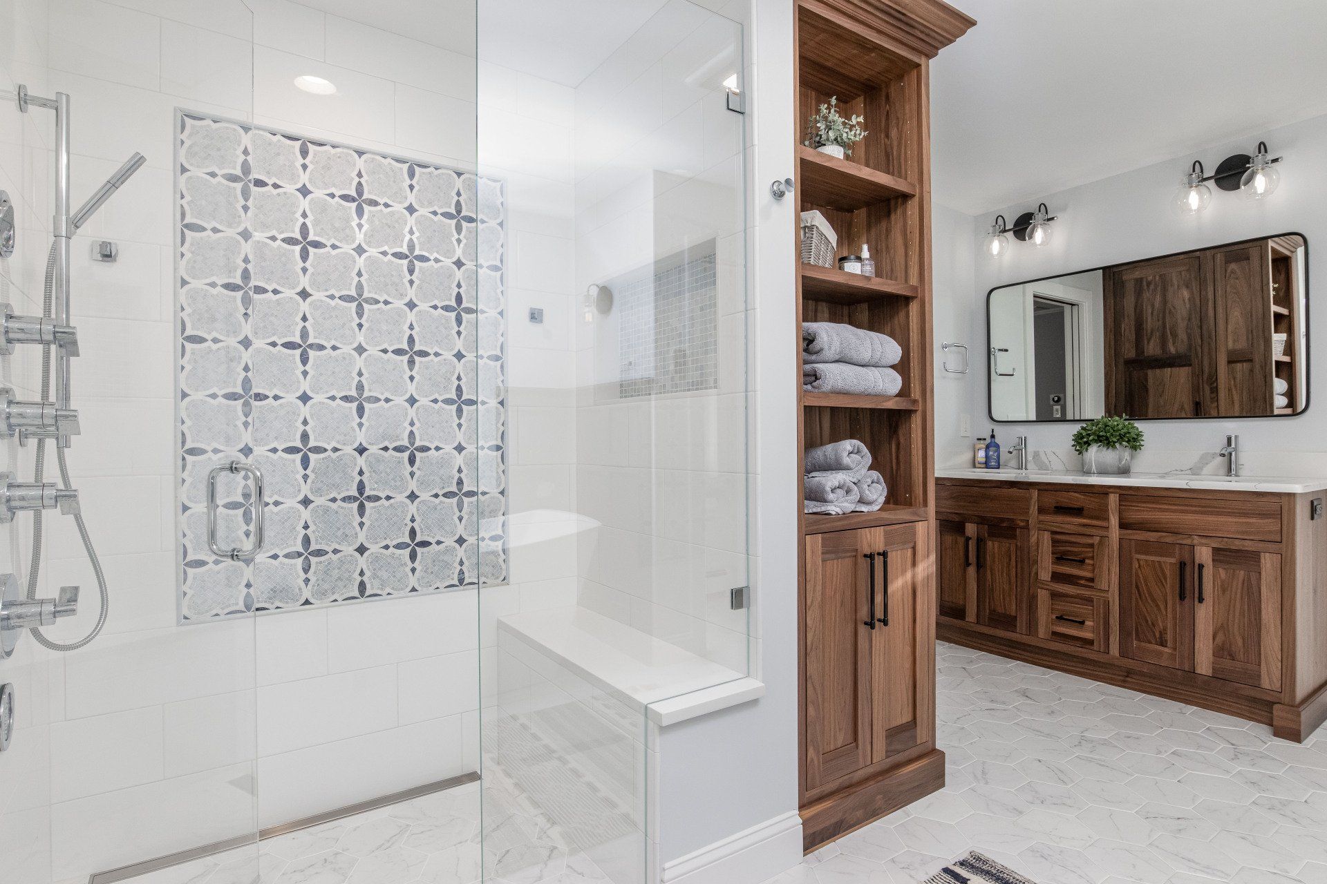 Modern bathroom with glass shower, patterned tile, and wooden vanity with mirror.