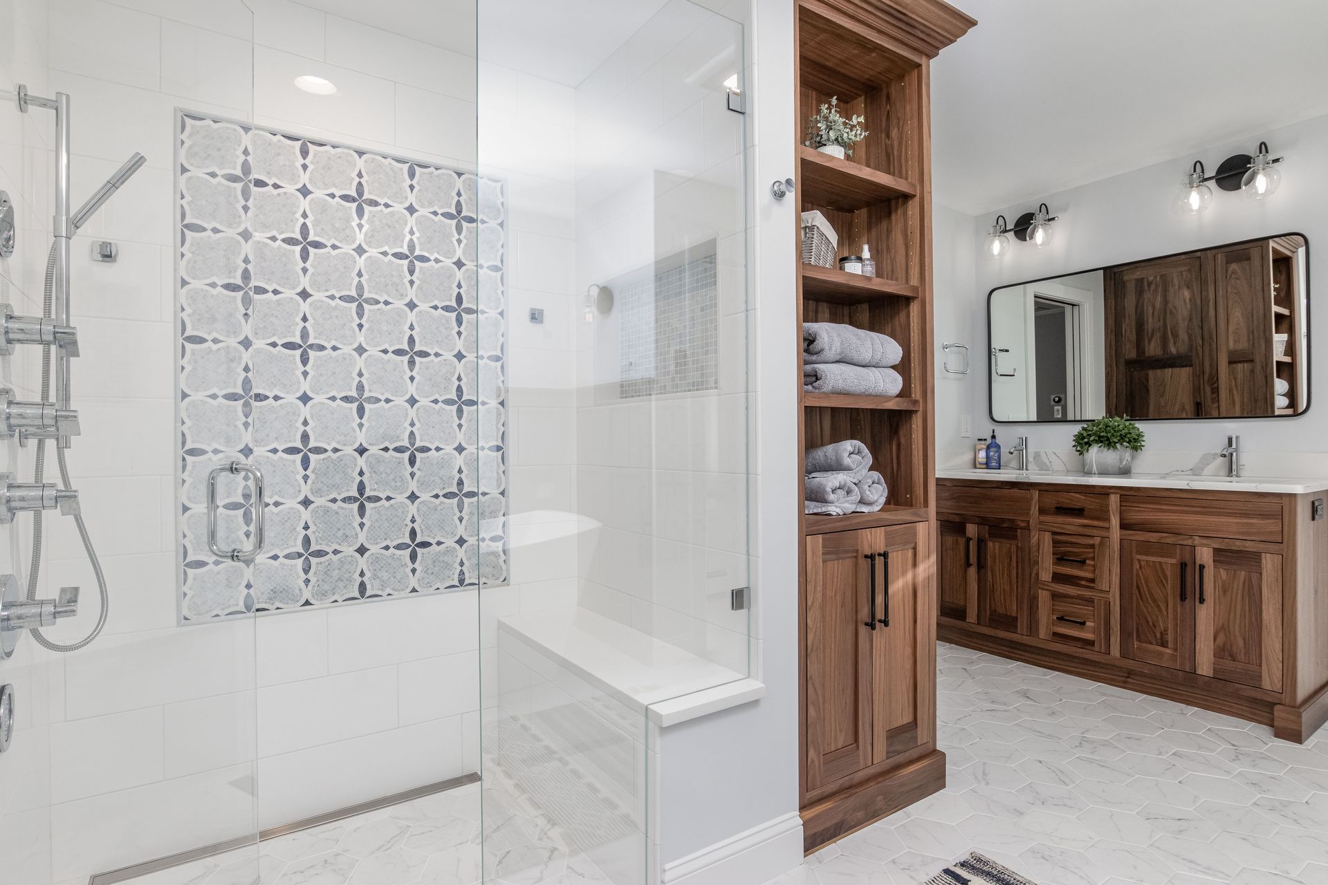 Modern bathroom with glass shower, patterned tile, and wood vanity with mirror and lights