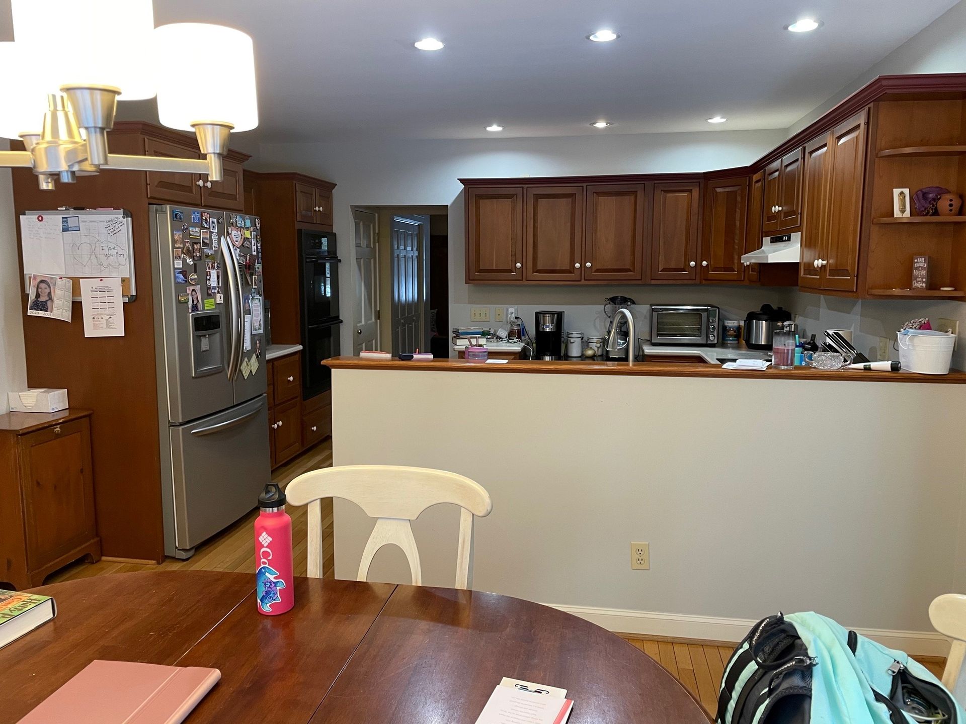 Kitchen and dining area with wooden cabinets, stainless steel fridge, and a table in the foreground.