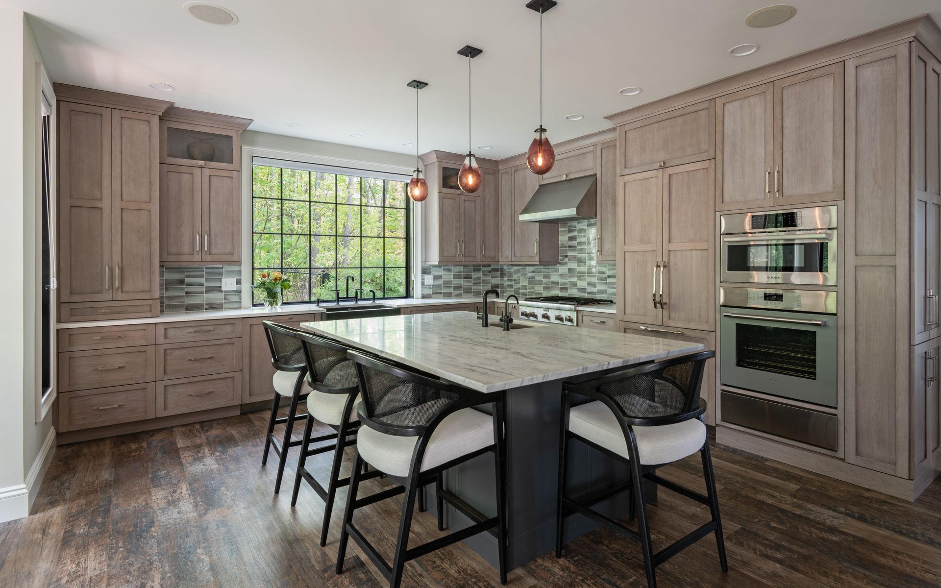 Modern kitchen with large island, black bar stools, light wood cabinets, and stainless steel appliances