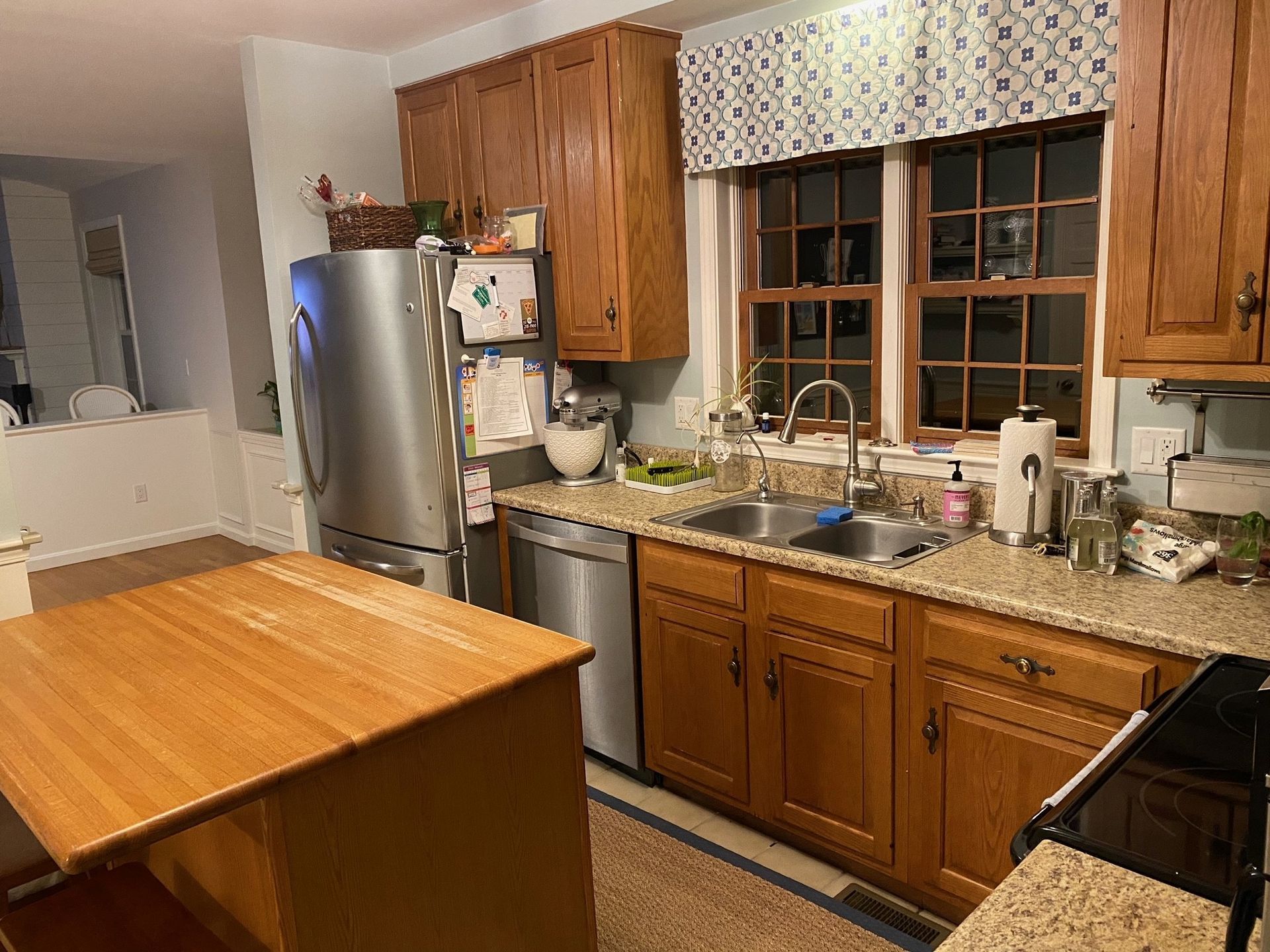 Kitchen with wood cabinets, stainless fridge, sink under window, and a large wooden island.