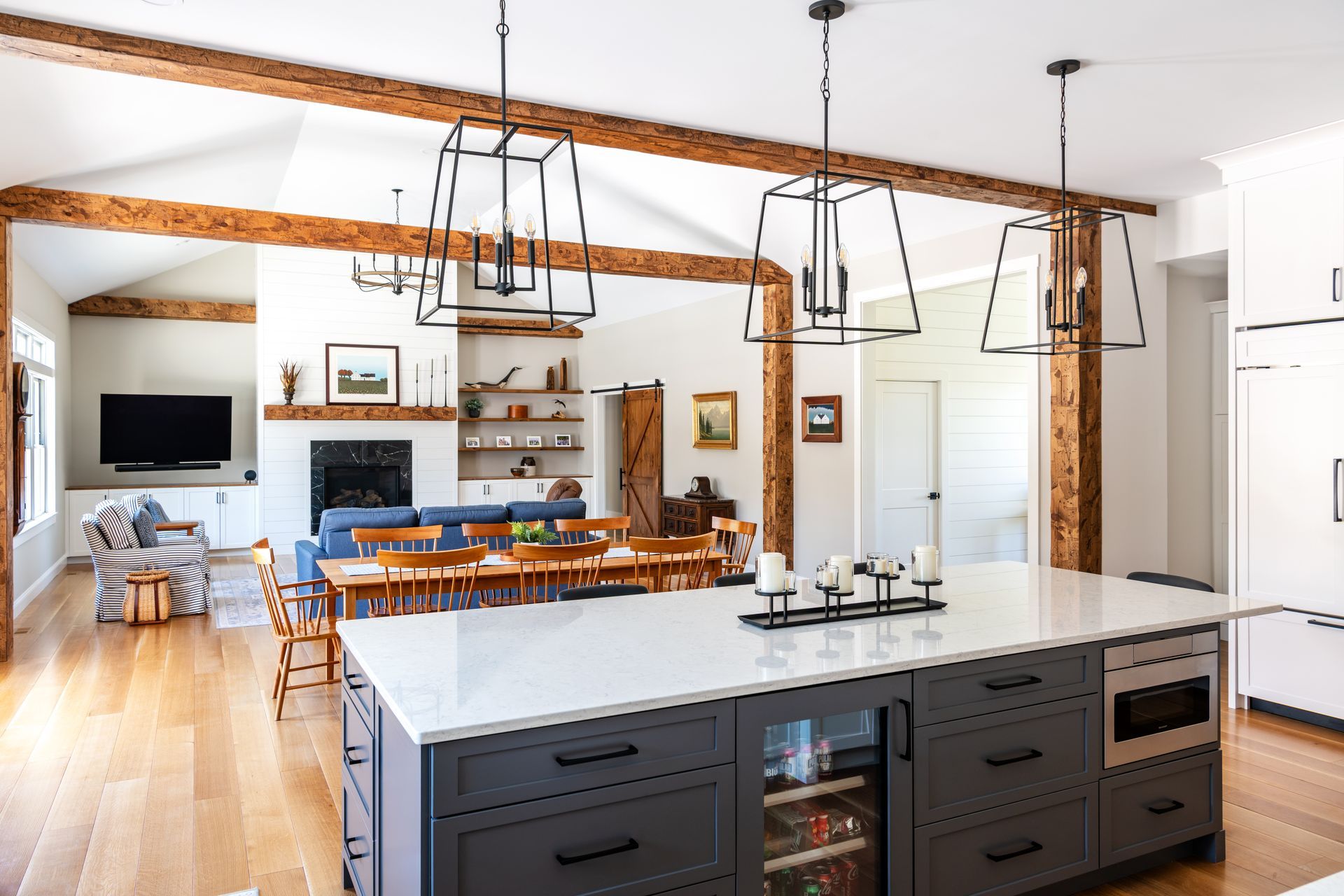 Modern kitchen with white island, dark cabinets, wood beams, and open dining/living area