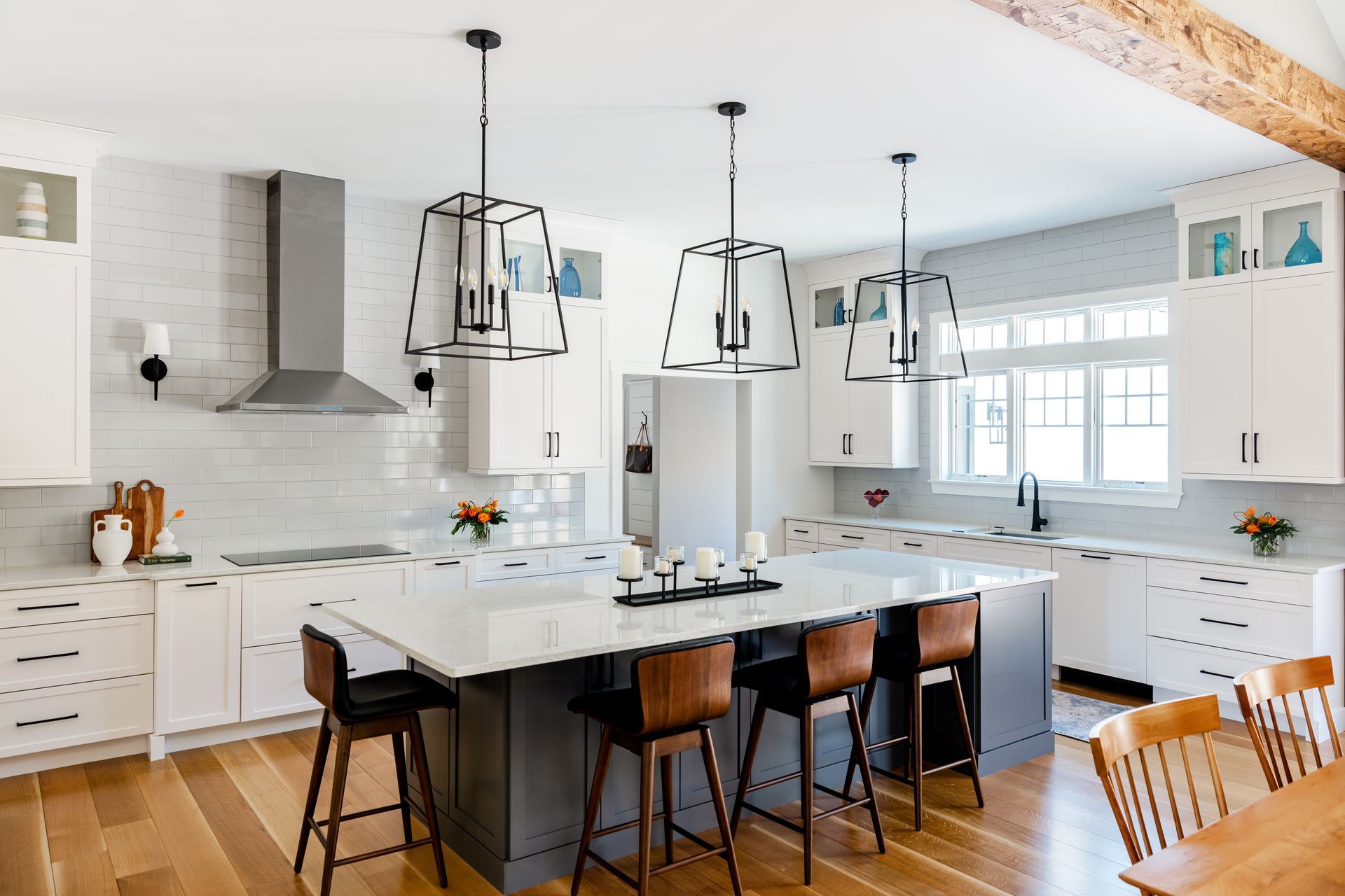 Bright modern kitchen with white cabinets, marble island, black barstools, and pendant lights