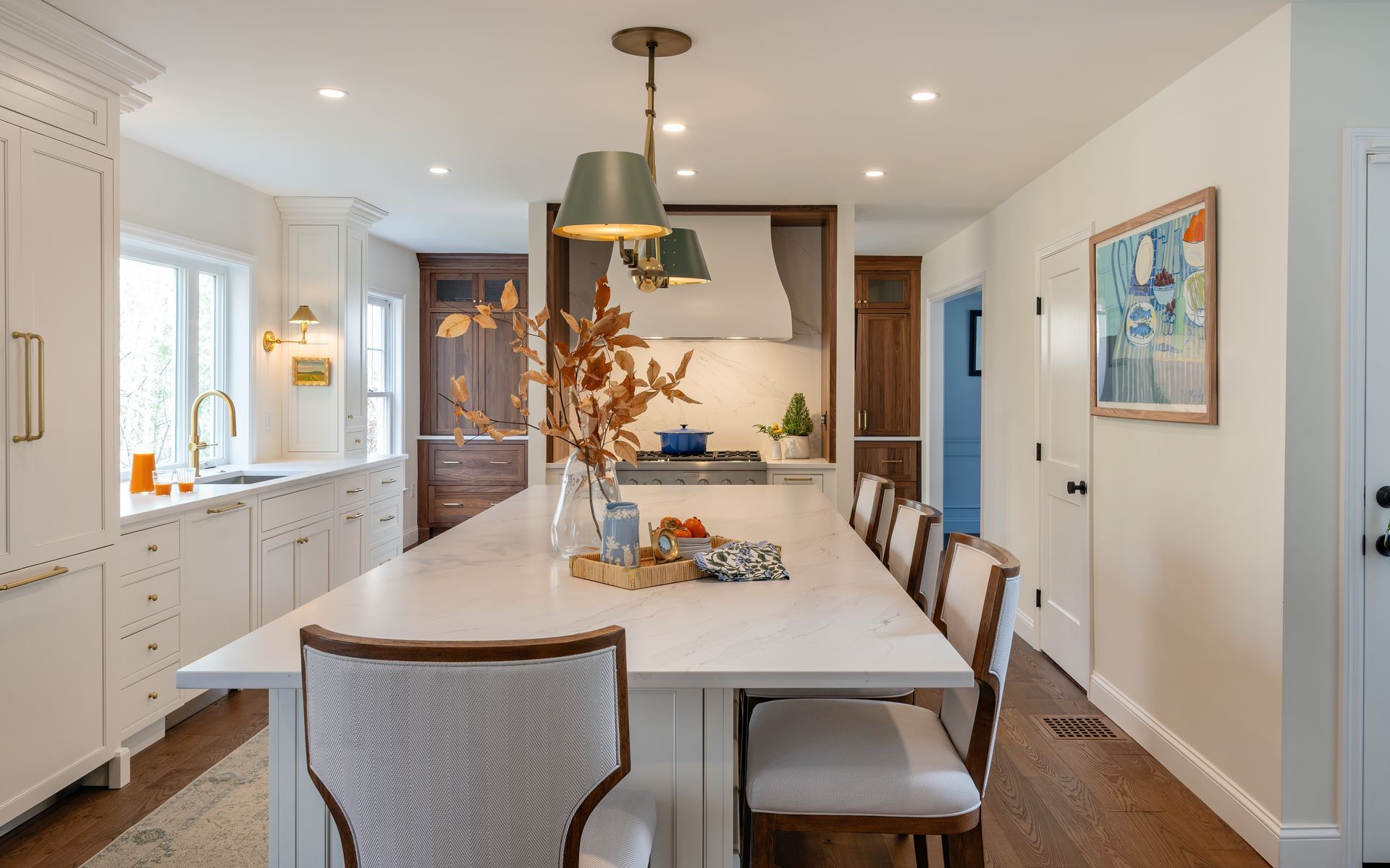 Bright modern kitchen with a large island, pendant lights, white cabinets, and a dining chair in the foreground
