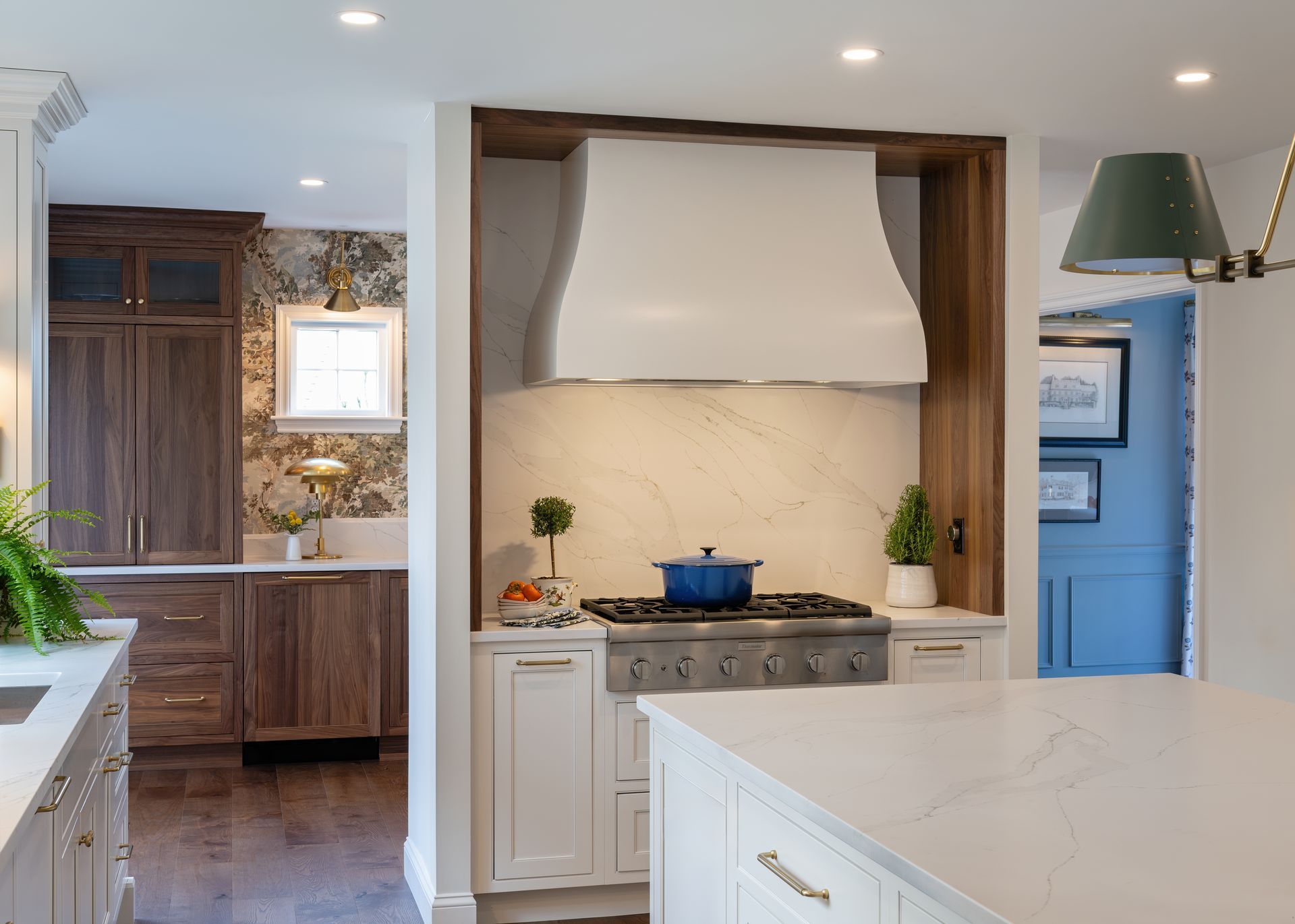Bright kitchen with a white stove hood, blue pot, island, and blue doorway accents